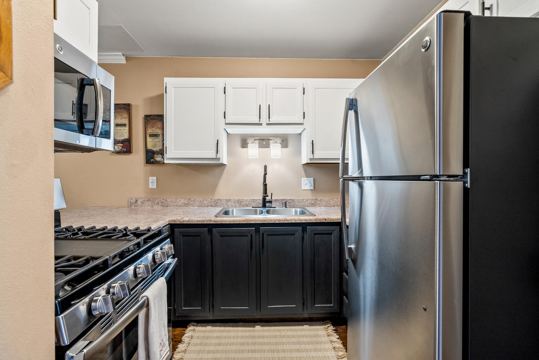 Compact kitchen with contrasting white and dark cabinets, stainless steel appliances, and a centered double-basin sink.