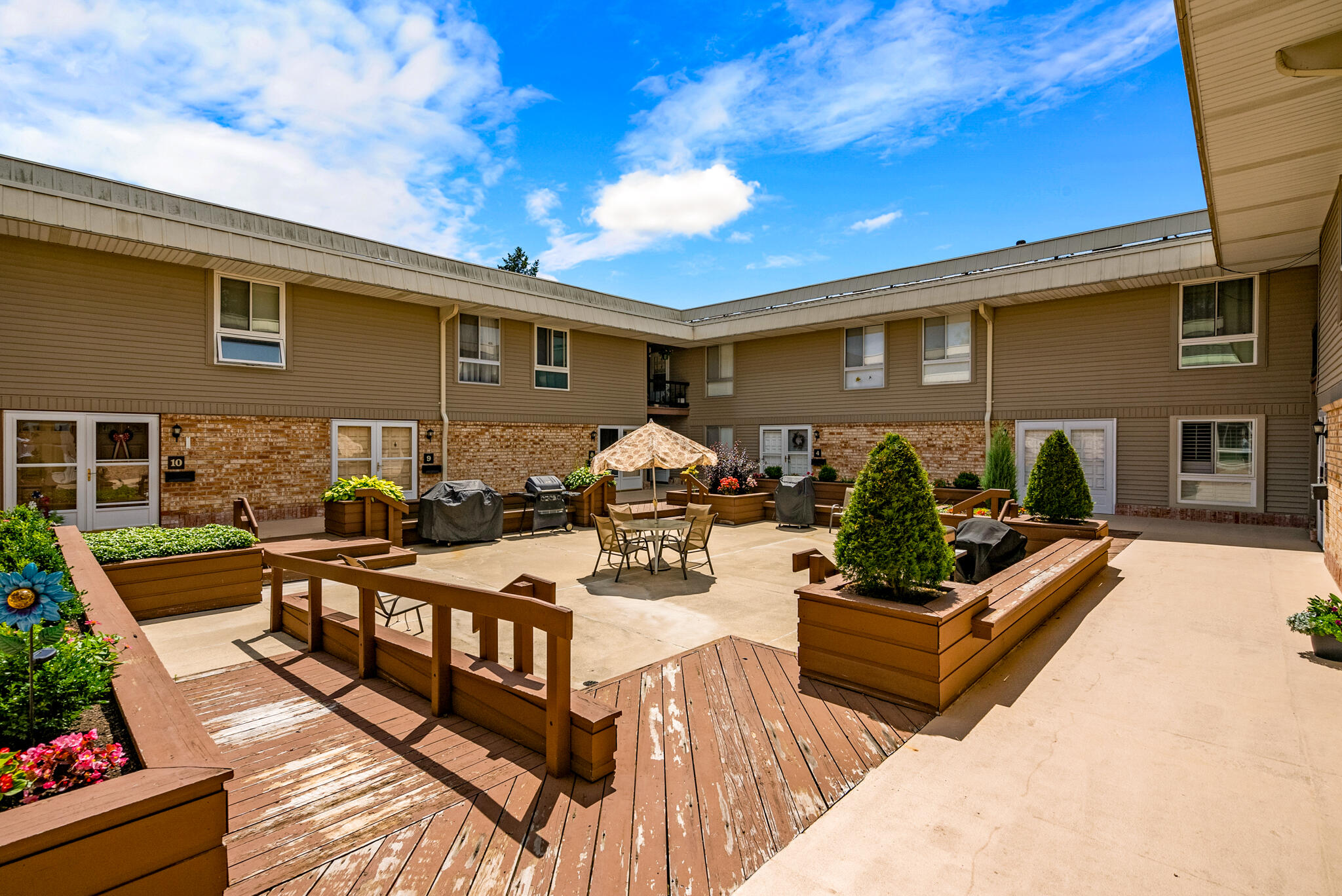 Condominium courtyard with raised planters, wooden decking, and outdoor seating beneath a patio umbrella.
