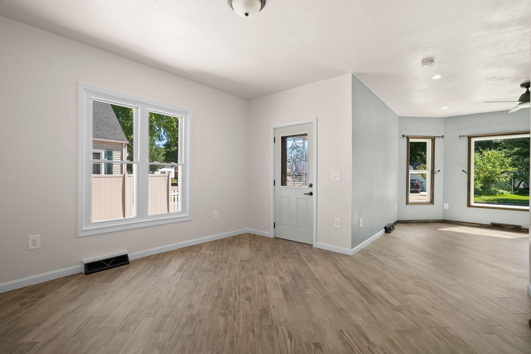Empty entry and living area with plank flooring, a decorative glass front door, and large windows.