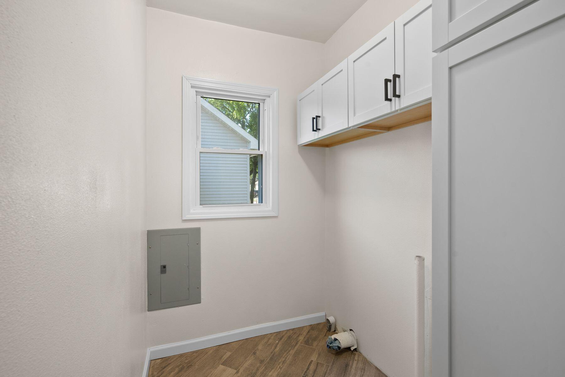 Empty utility room with white cabinets, a window, and wood-look flooring.