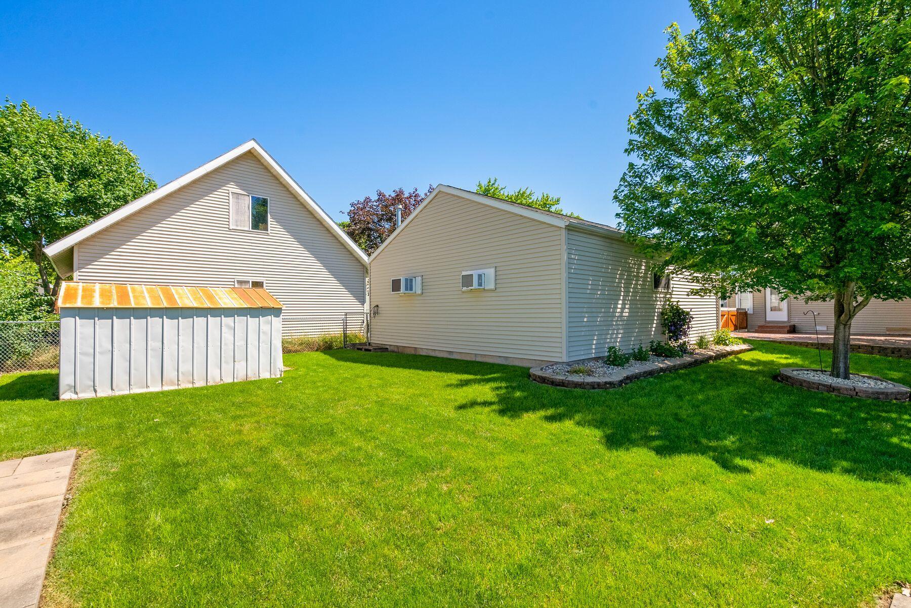 Beige-sided home and side yard with a metal shed, green lawn, and mature trees.