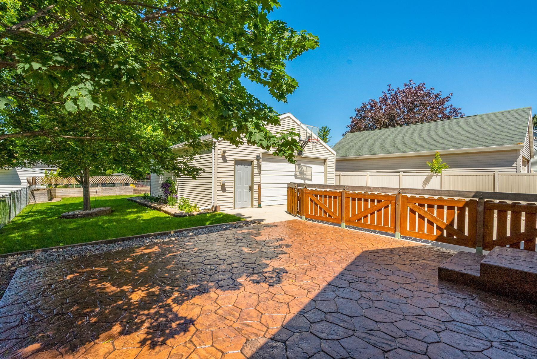 Backyard patio with stamped concrete, fenced lawn, shade tree, and detached garage with basketball hoop.