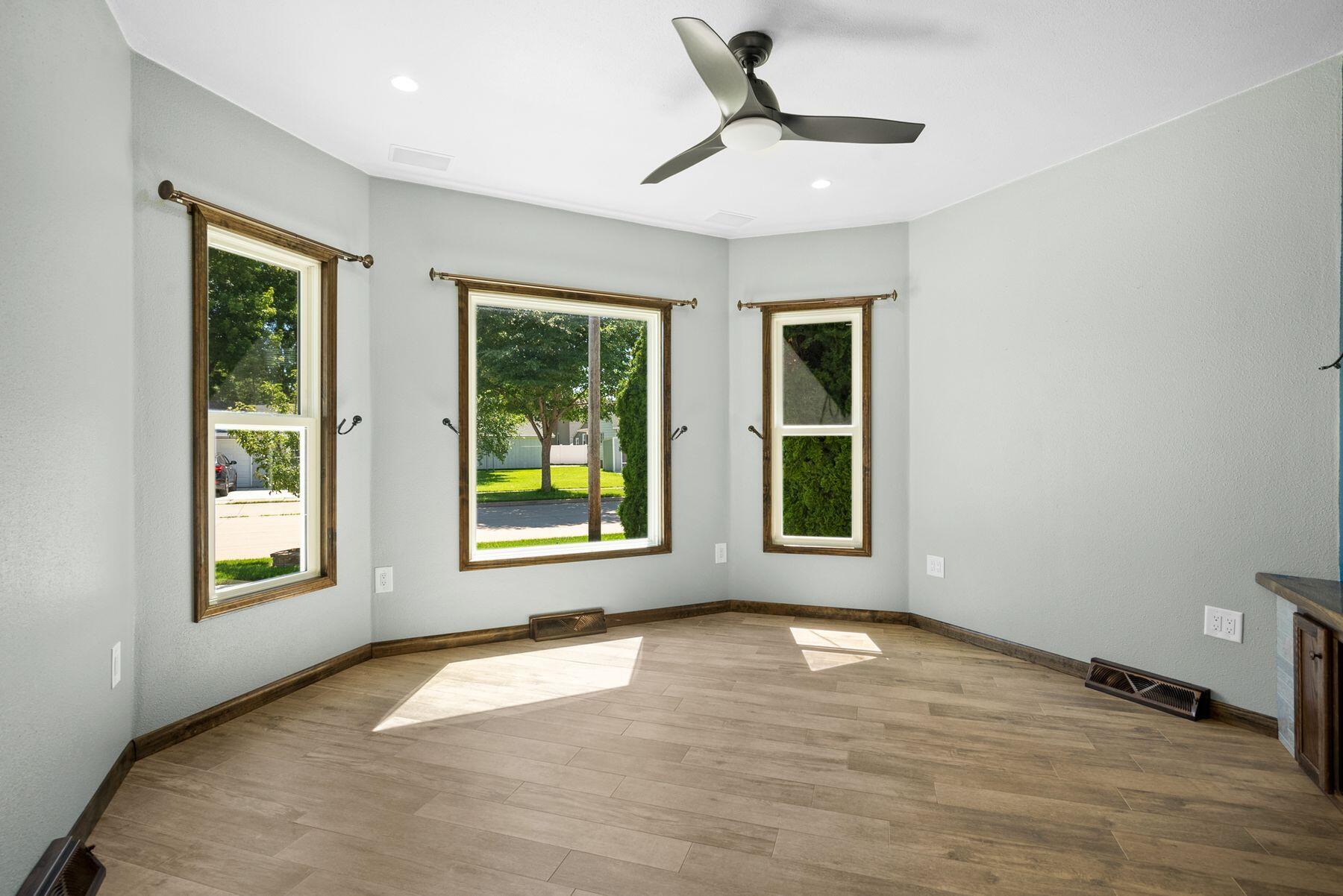 Empty room with wood-look tile floors, three windows, and a ceiling fan.