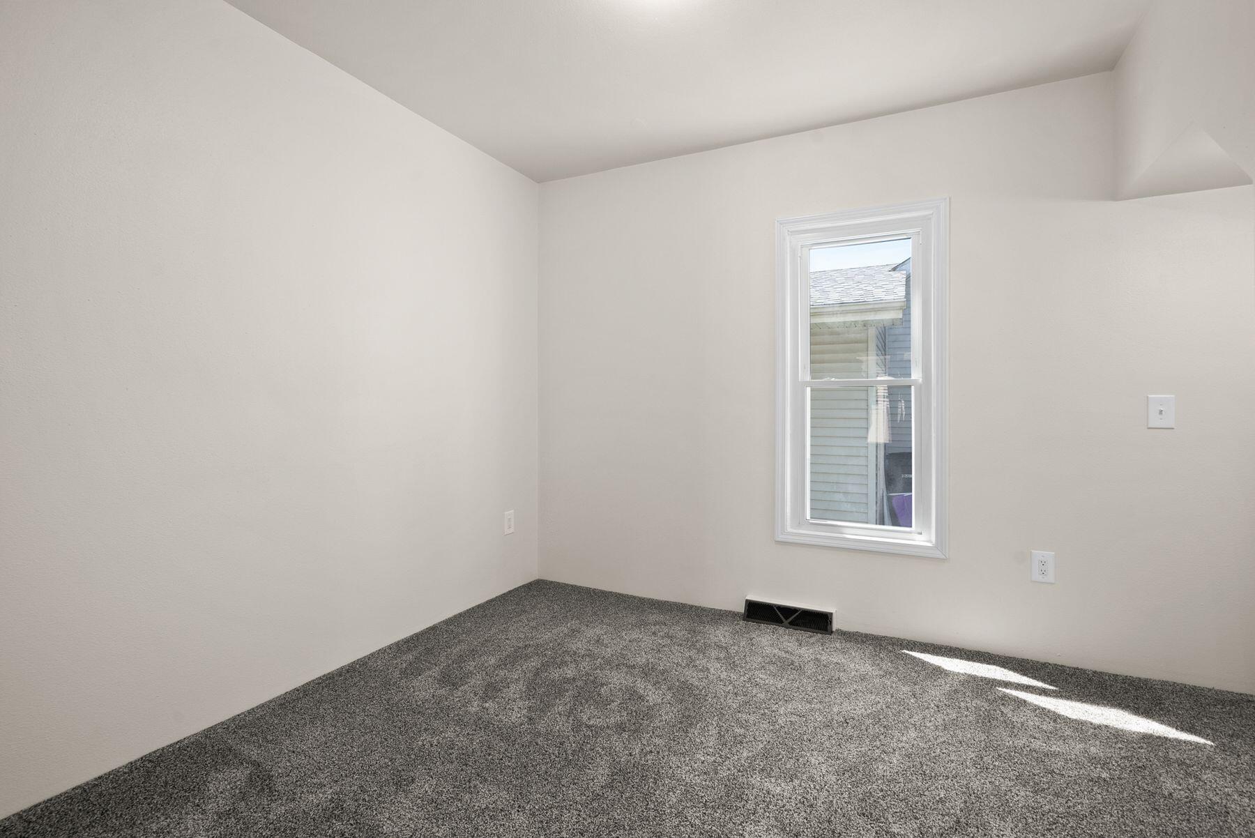 Empty bedroom with dark gray carpet, a single window, and sunlight on the floor.