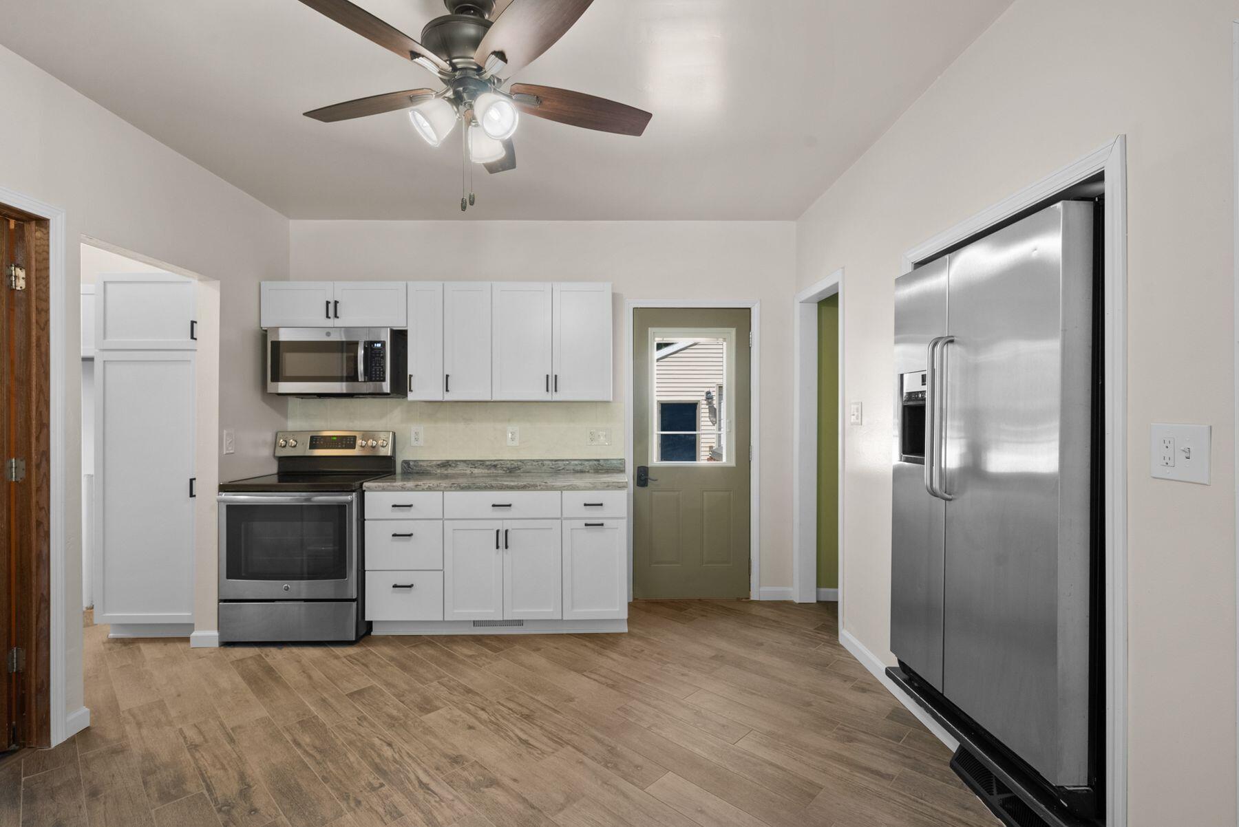 Kitchen with white cabinetry, stainless steel appliances, and wood-look tile flooring.