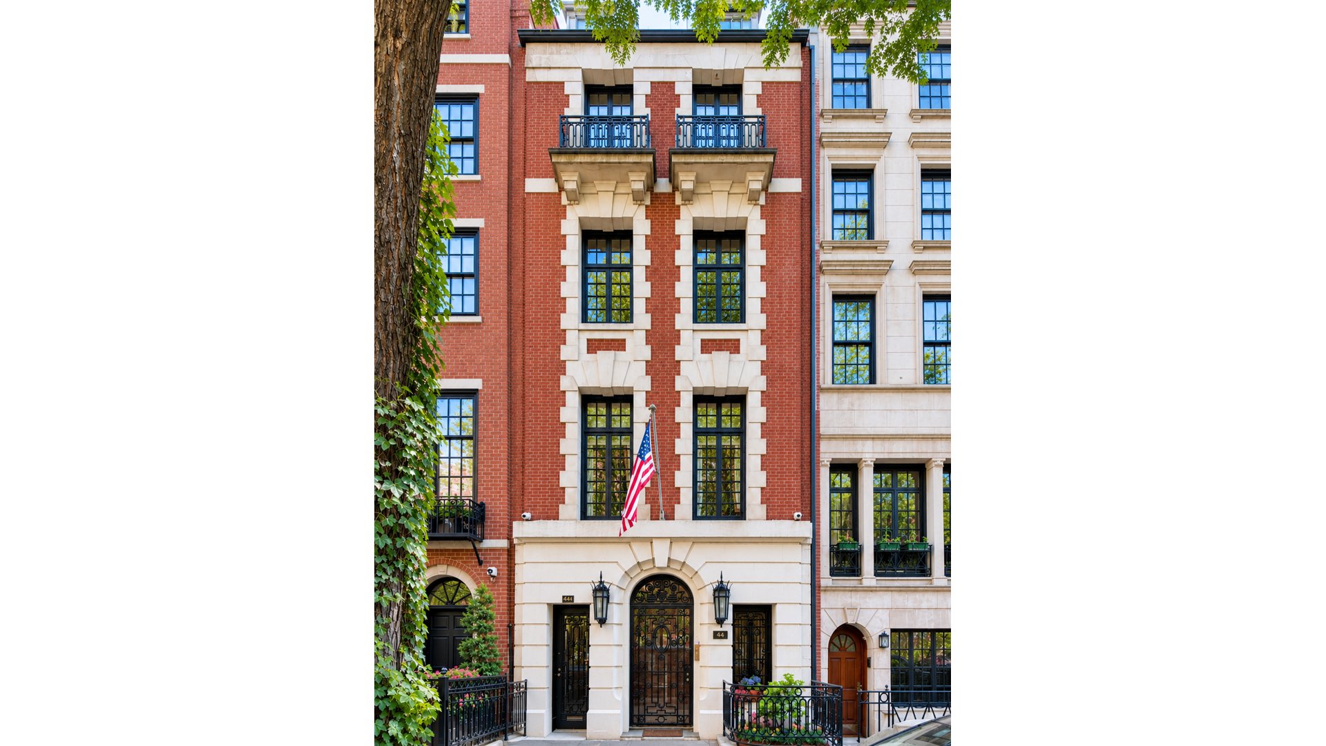 Red-brick townhouse with ornate stone trim, wrought-iron entry gates, and an American flag.