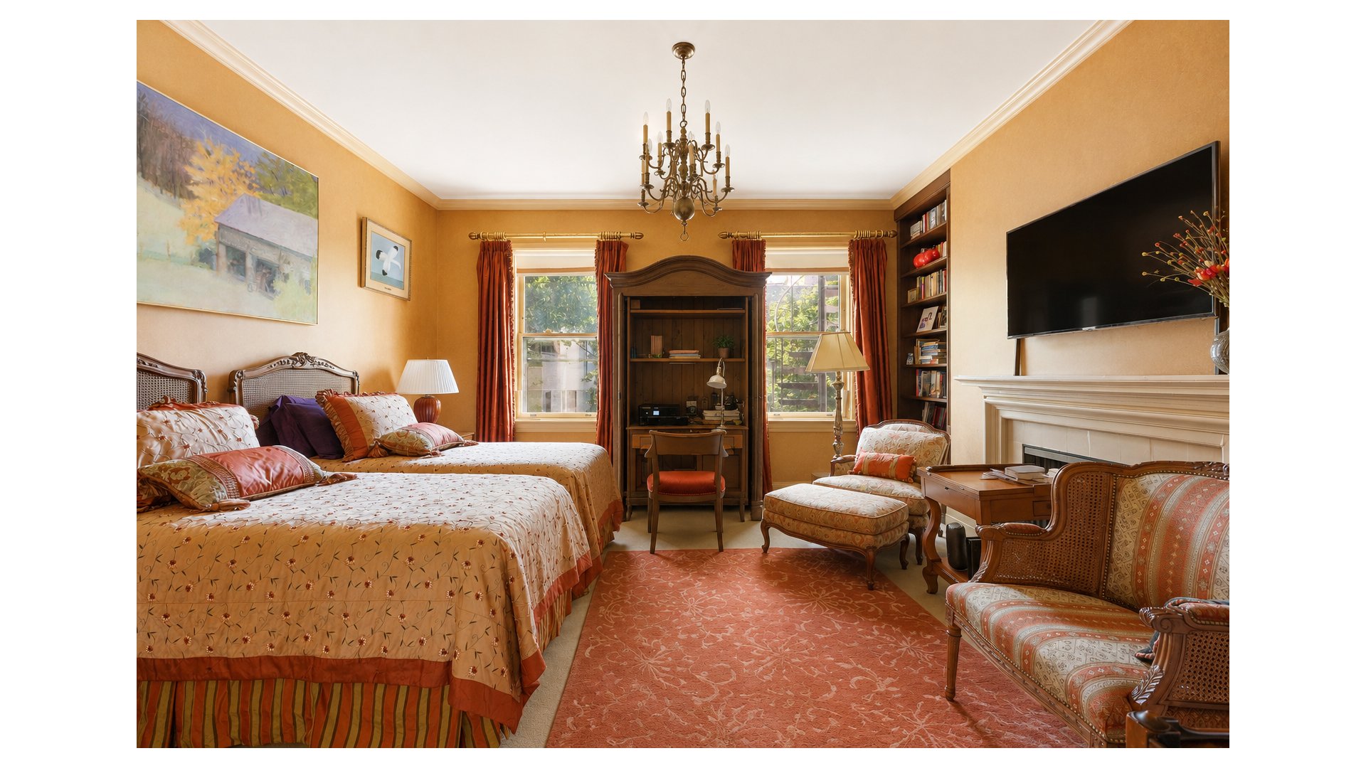 Bedroom with two patterned beds, a built-in desk between windows, and a fireplace beneath a television.