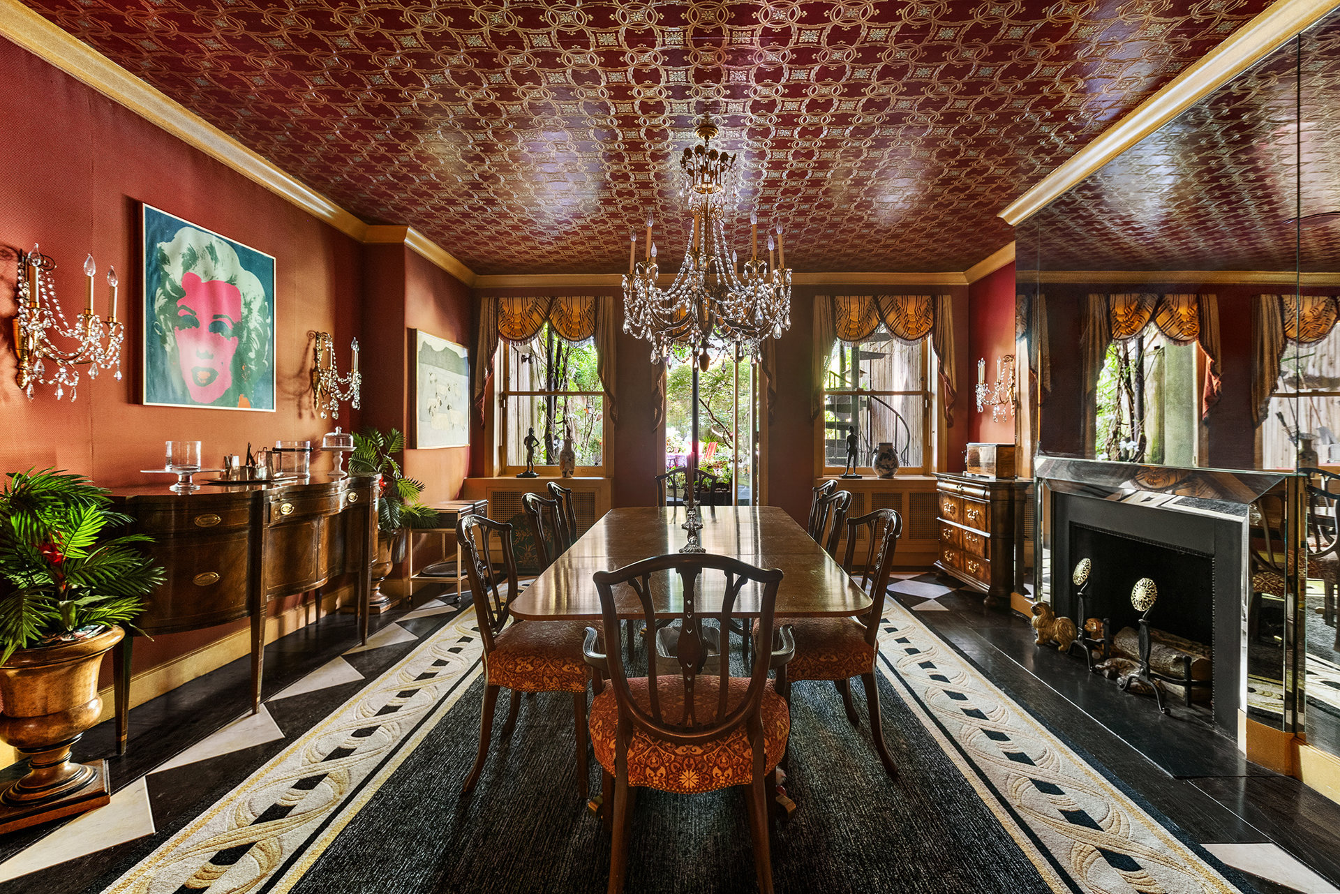 Dining room with a long table, crystal chandeliers, ornate ceiling, and mirrored fireplace.