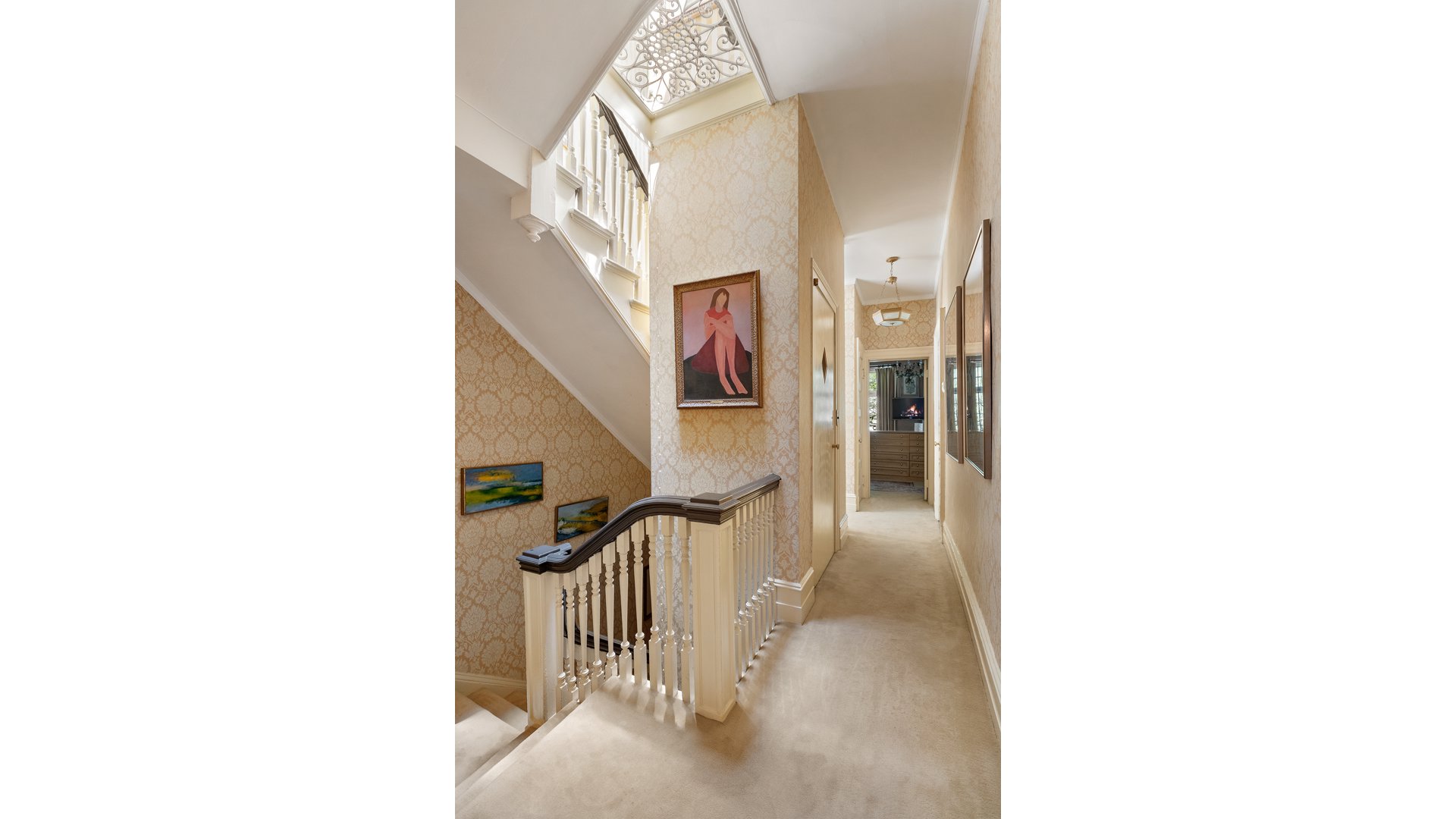 Carpeted upstairs hallway beside a staircase, with patterned wallpaper and a decorative skylight.