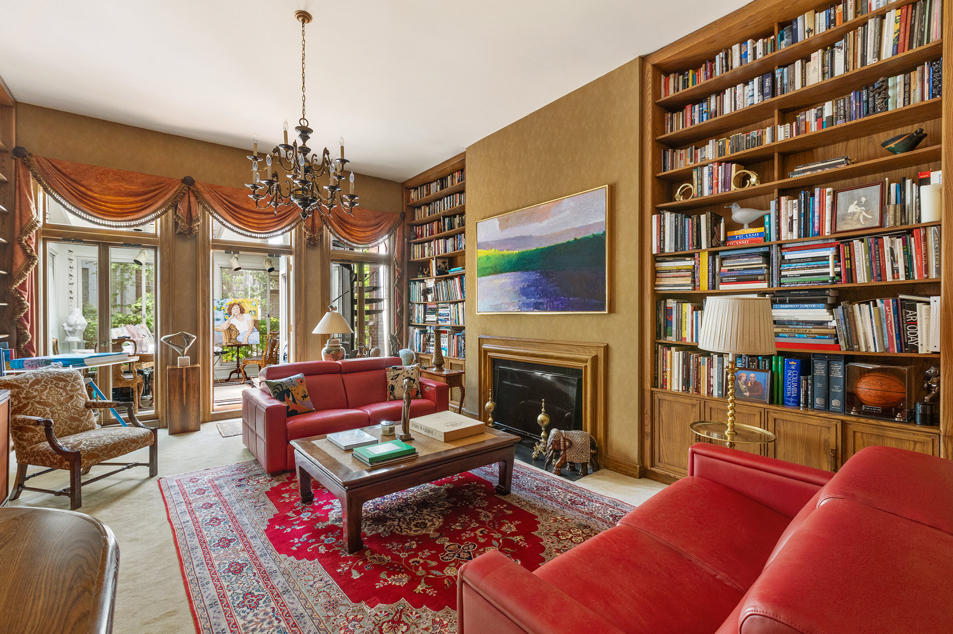 Living room with wall-to-wall bookshelves, a fireplace, red leather sofas, and tall draped windows.