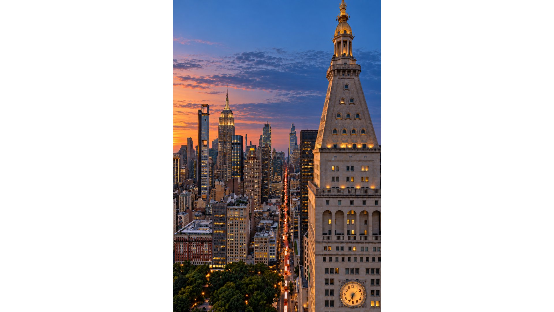 Manhattan skyline at dusk with the Empire State Building and a clock tower overlooking Madison Square Park.