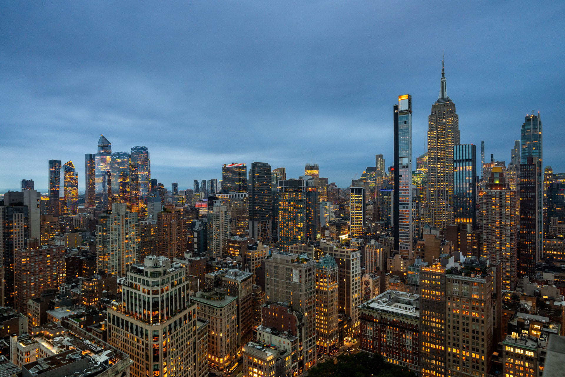 Manhattan skyline at dusk, with the illuminated Empire State Building rising above surrounding skyscrapers.
