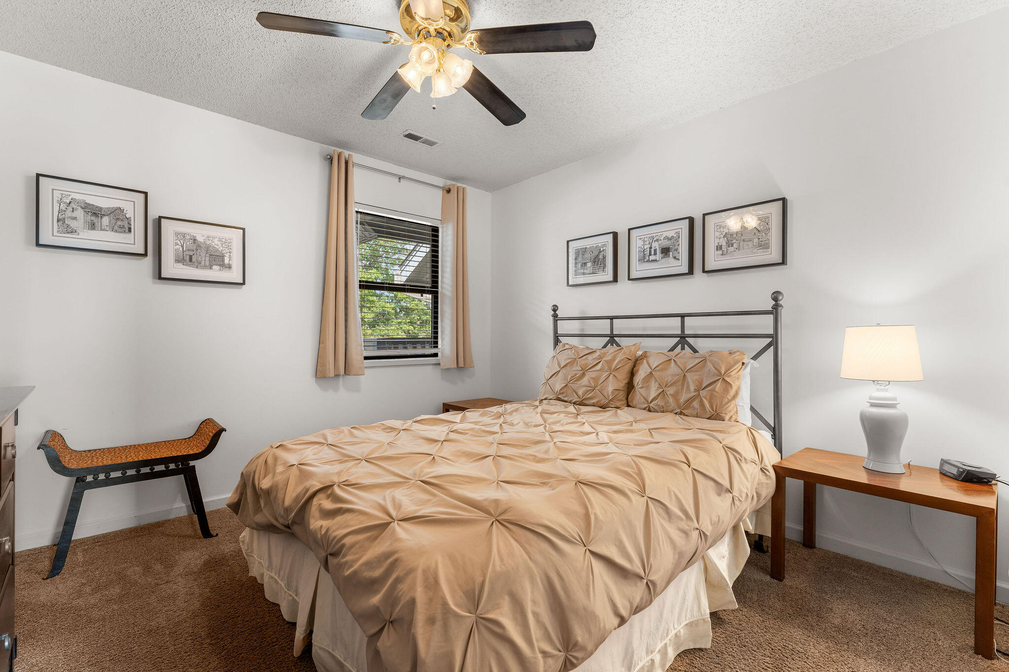 Bedroom with tan geometric bedding, a dark metal bed frame, framed prints, and a window with beige curtains.