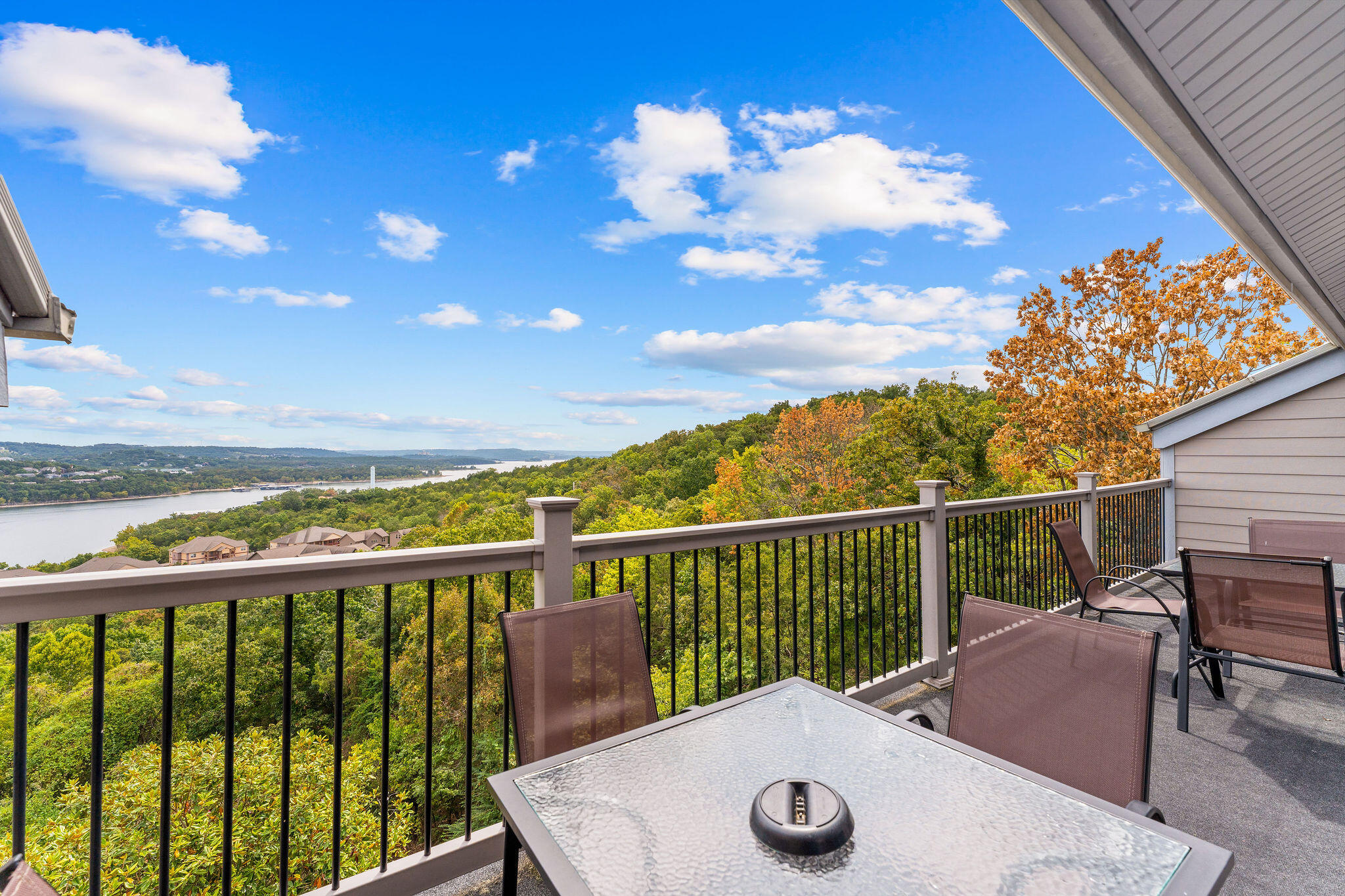 Deck with patio furniture overlooking wooded hills and water.