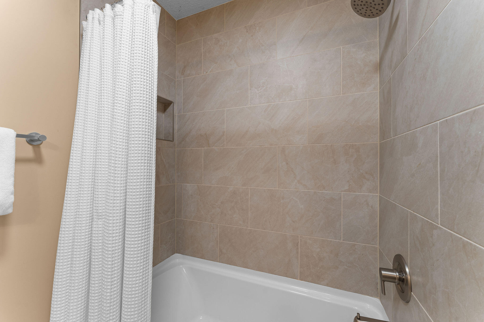 Bathroom tub and shower with beige tile, a white curtain, and brushed-metal fixtures.