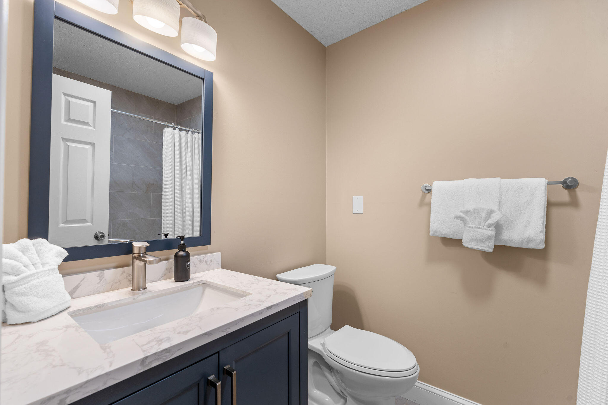 Bathroom with a dark blue vanity, marble-look counter, large mirror, and white towels.