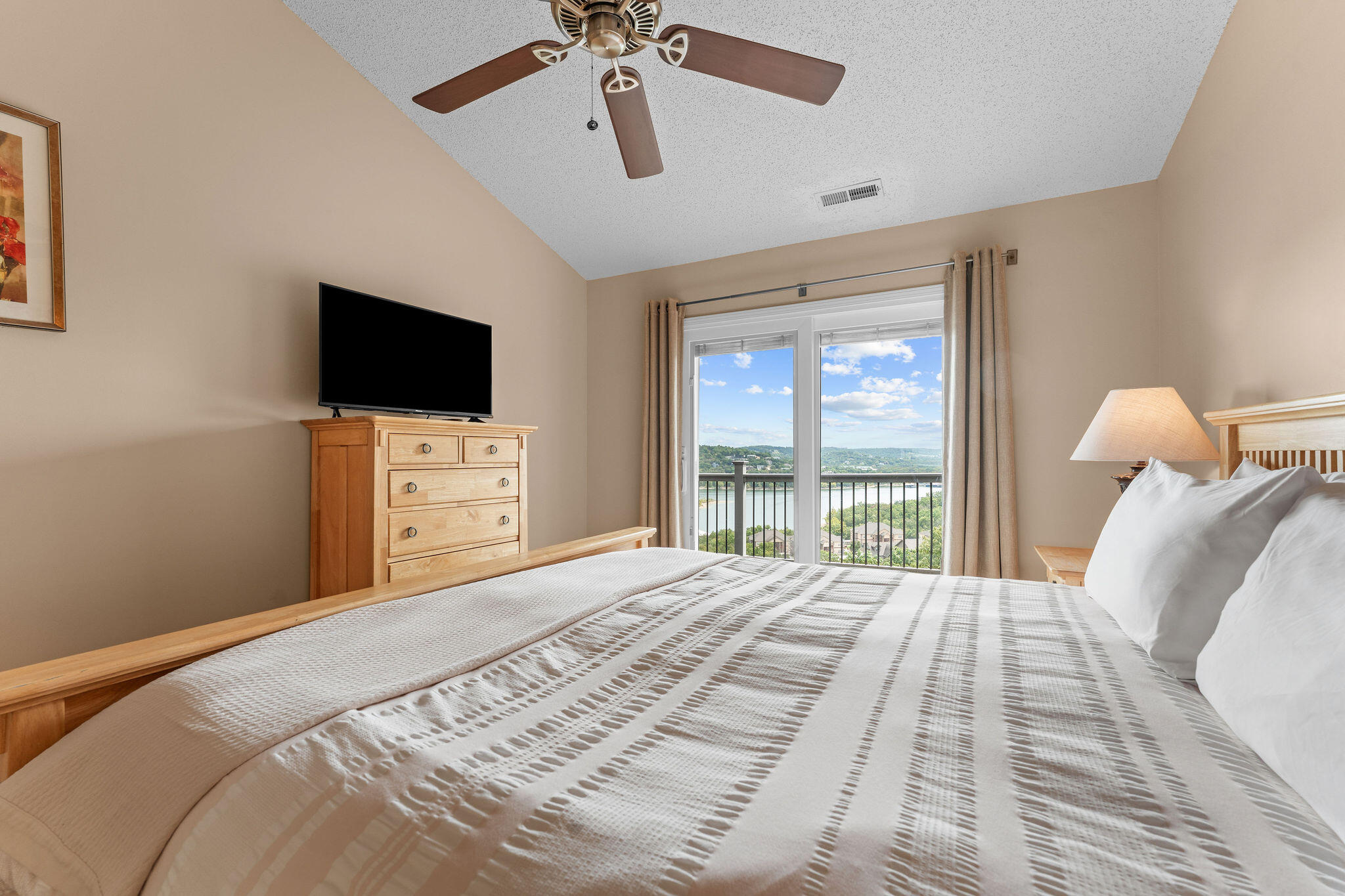 Bedroom with a large bed and balcony doors overlooking water and wooded hills.