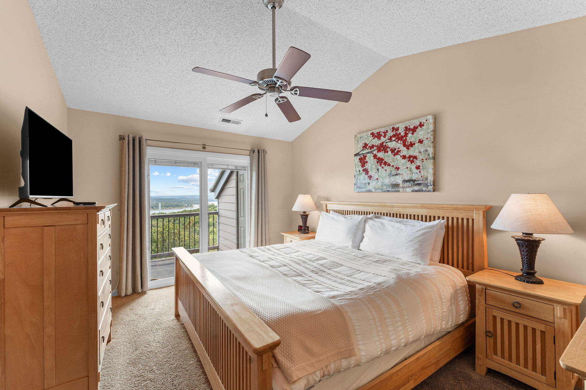 Bedroom with a wooden bed and balcony doors overlooking water and wooded hills.