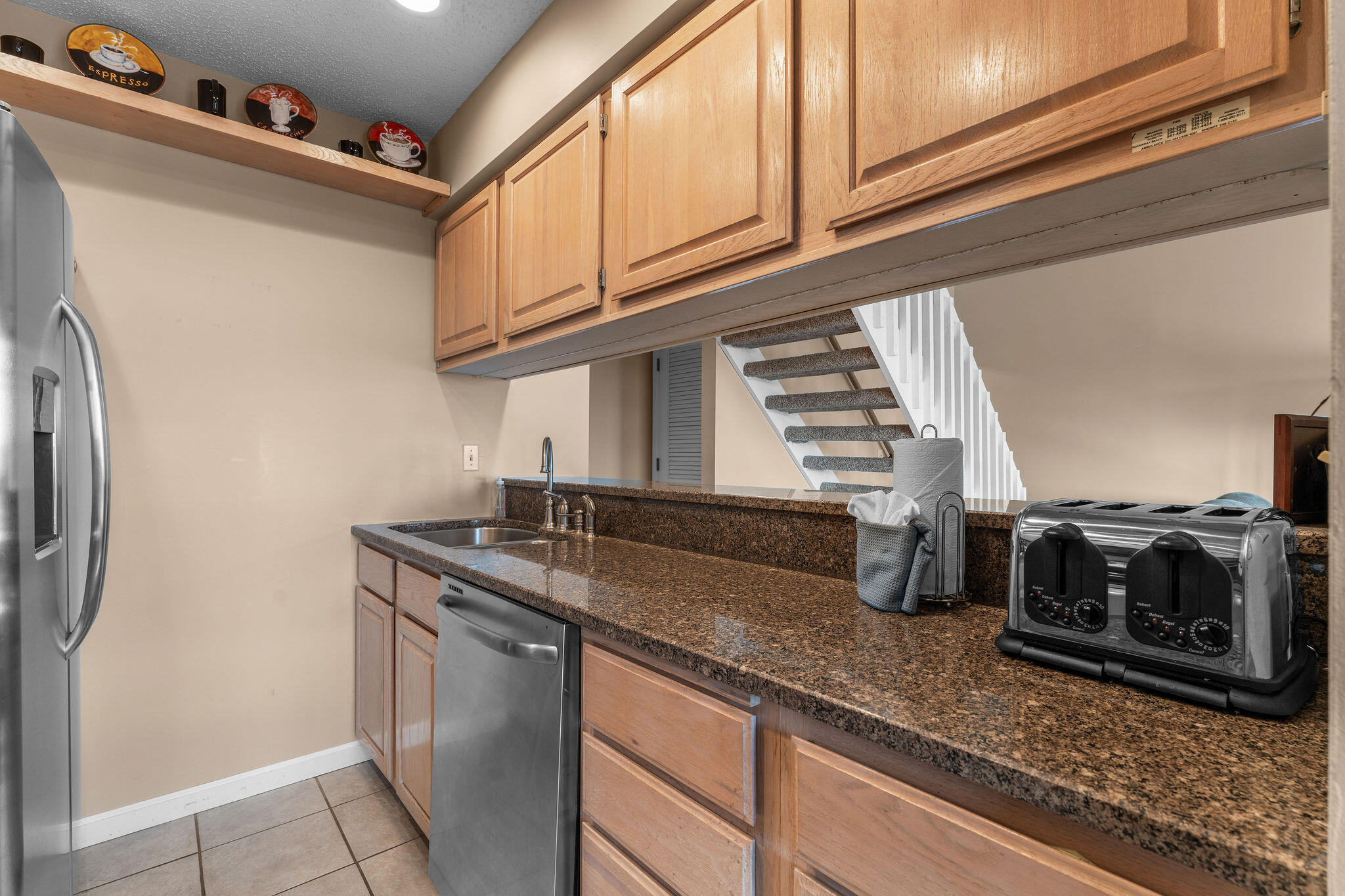Kitchen with granite counters, wood cabinets, stainless appliances, and stairs behind the counter.