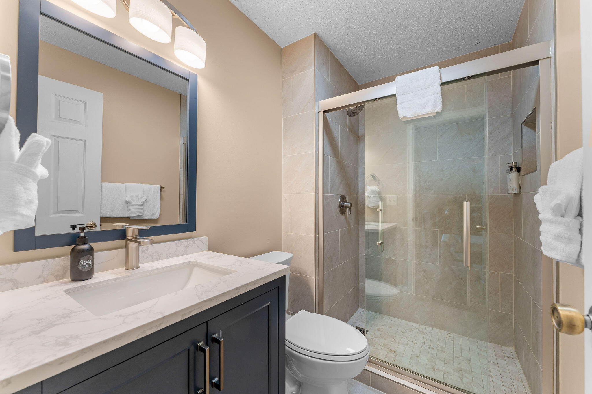 Bathroom with a glass-tiled shower, dark vanity, marble-look countertop, and white towels.