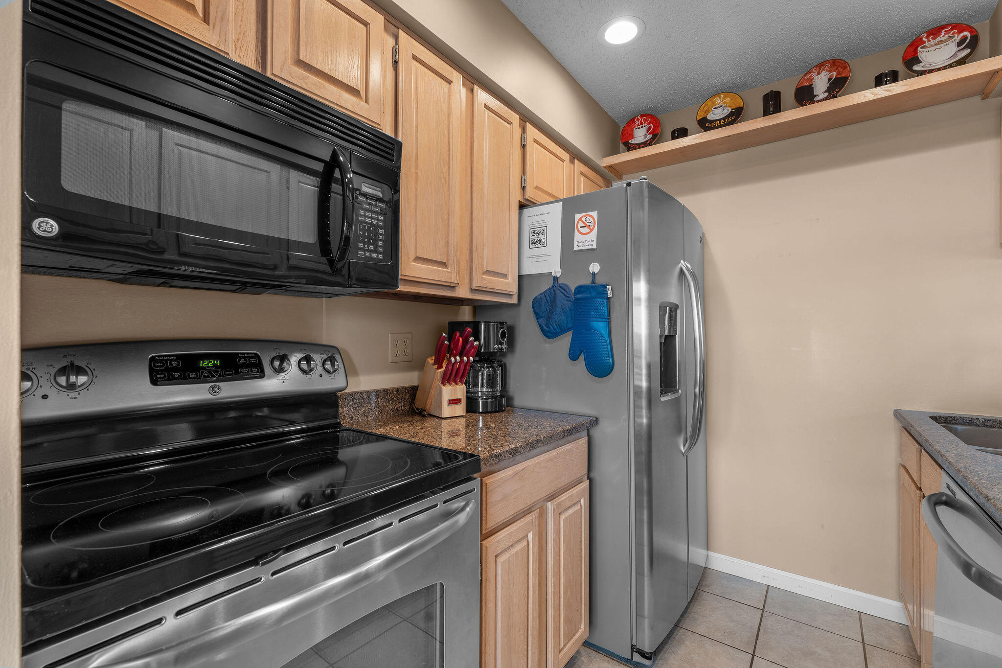 Kitchen with light wood cabinets, granite counters, and stainless steel refrigerator beside a black electric range.