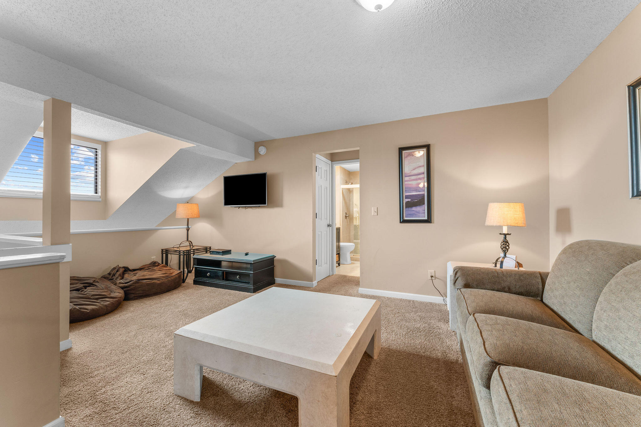 Furnished living area with a sofa, beanbag chairs, and a television beneath a sloped ceiling.