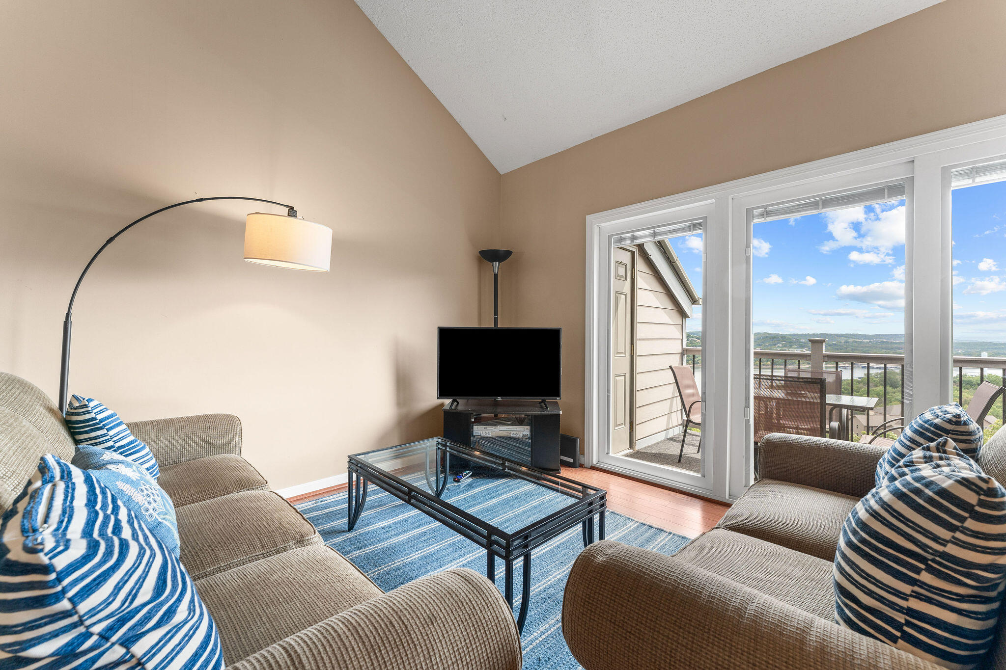 Furnished living room with blue accents and sliding doors opening to a balcony overlooking water.