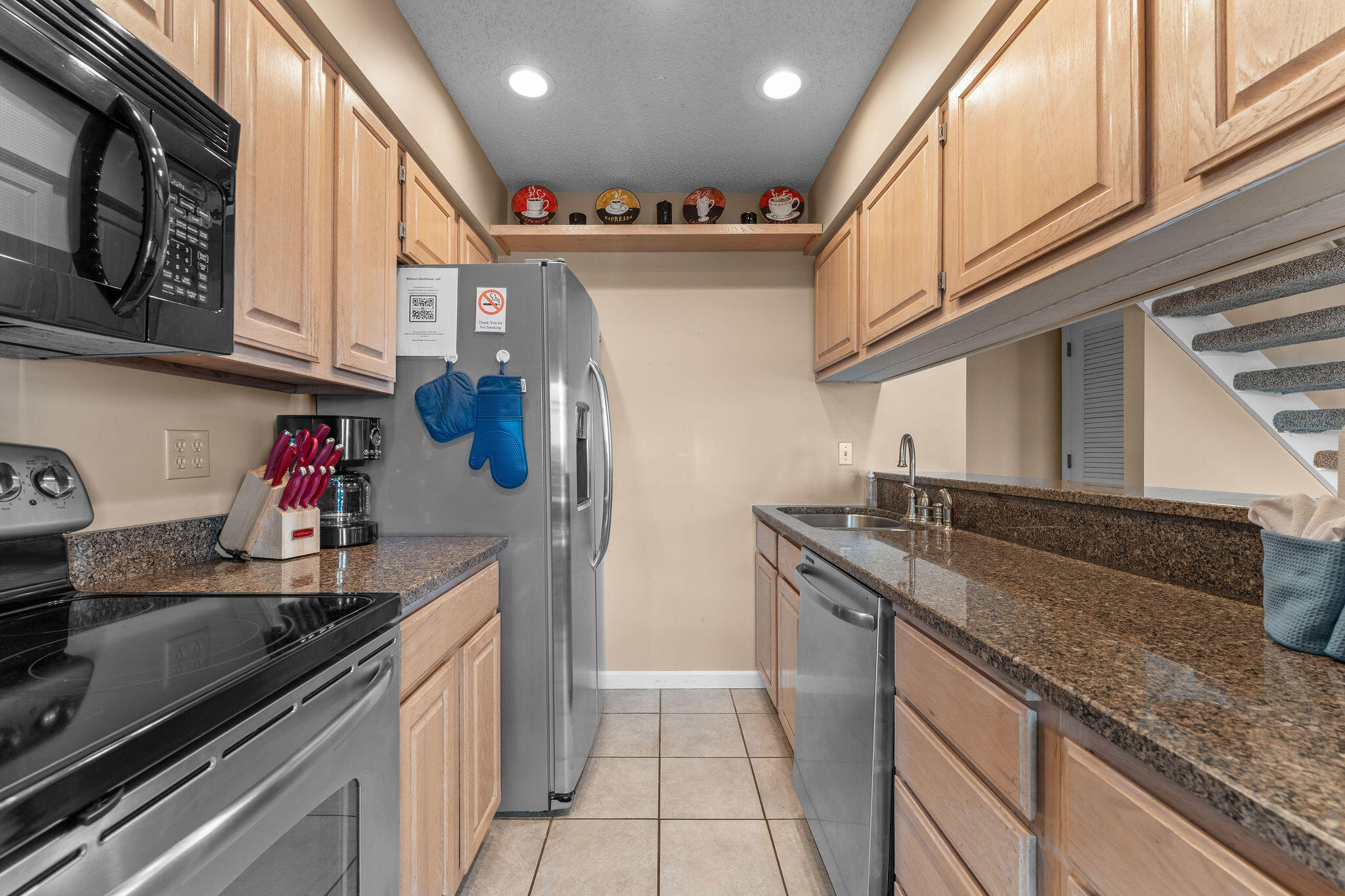 Kitchen with light wood cabinets, granite counters, stainless steel appliances, and a staircase along the right side.