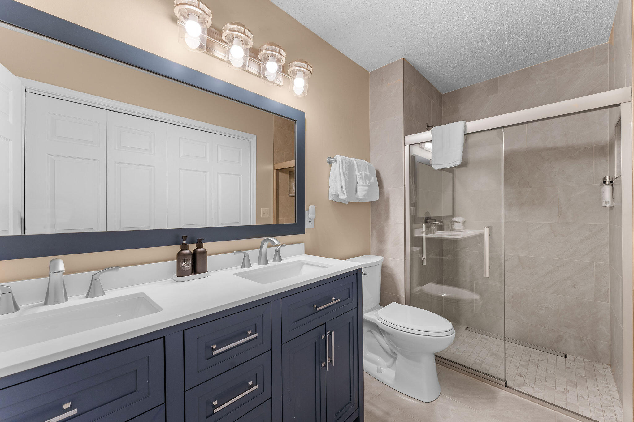 Bathroom with a dark blue double vanity and a tiled glass-enclosed shower.