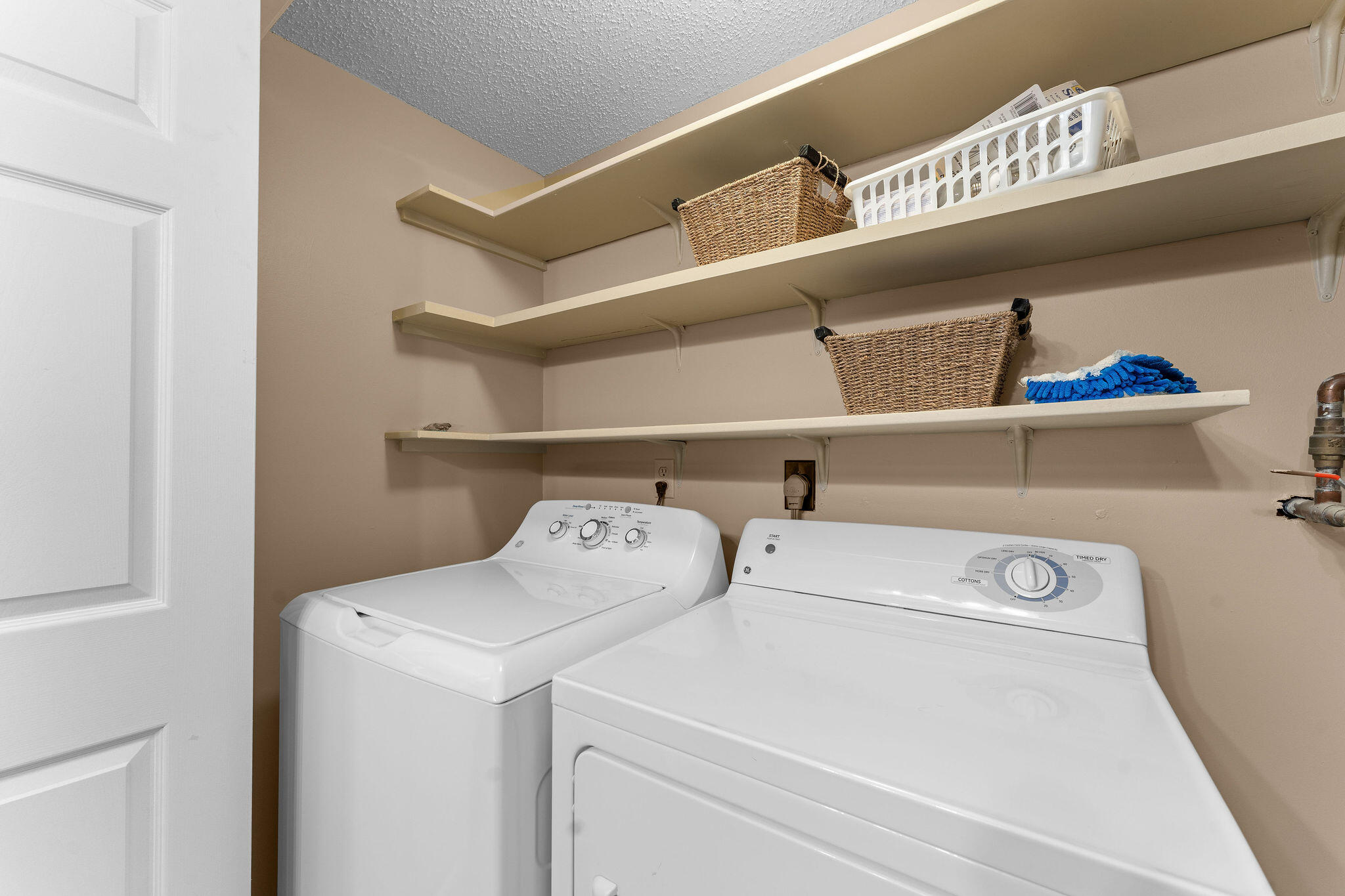 Laundry room with white washer and dryer beneath shelves holding wicker baskets.