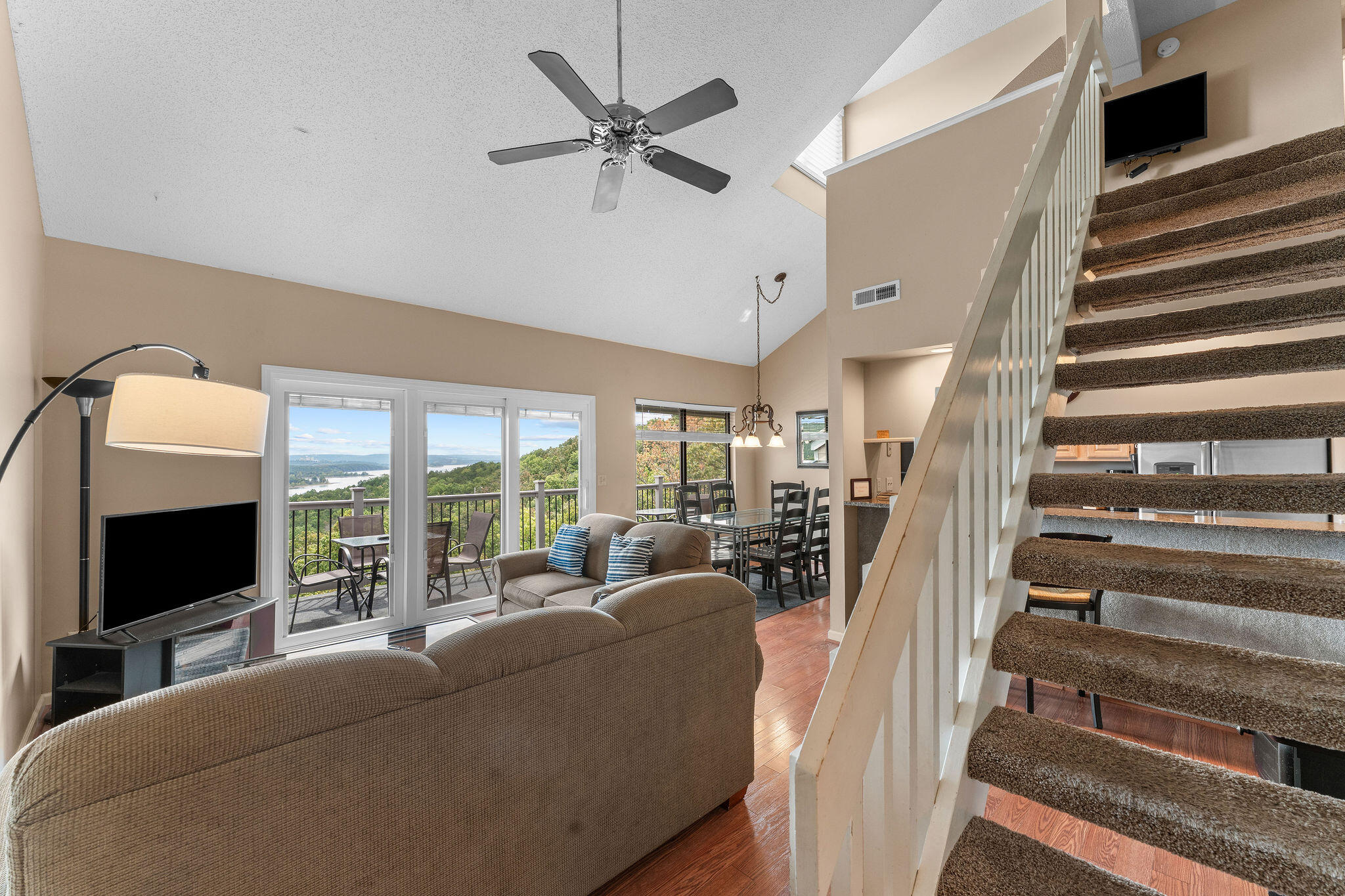 Open-plan living and dining area with a carpeted staircase and balcony overlooking a lake.