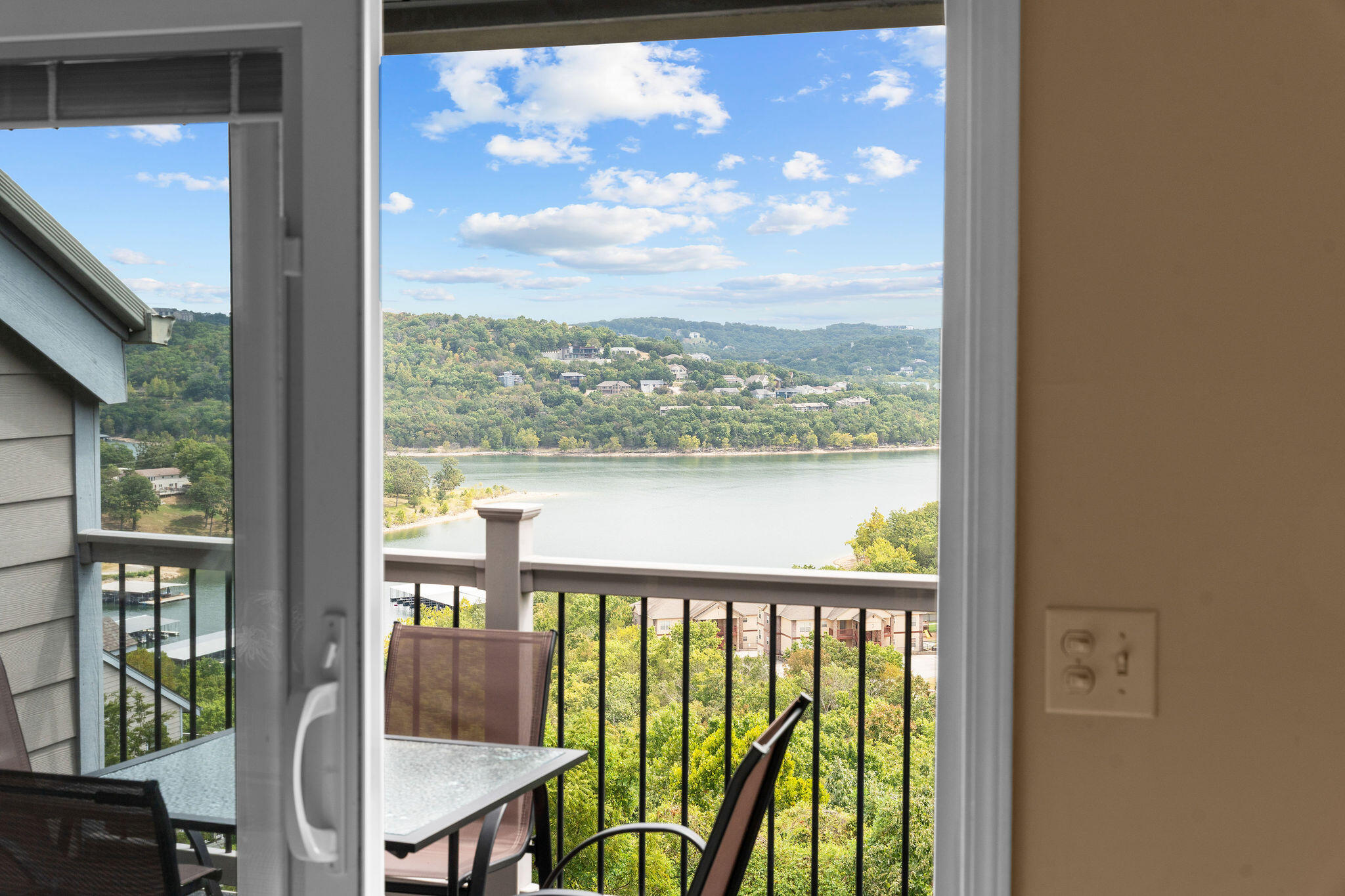 Lake and wooded shoreline viewed from a condo balcony furnished with a table and chairs.