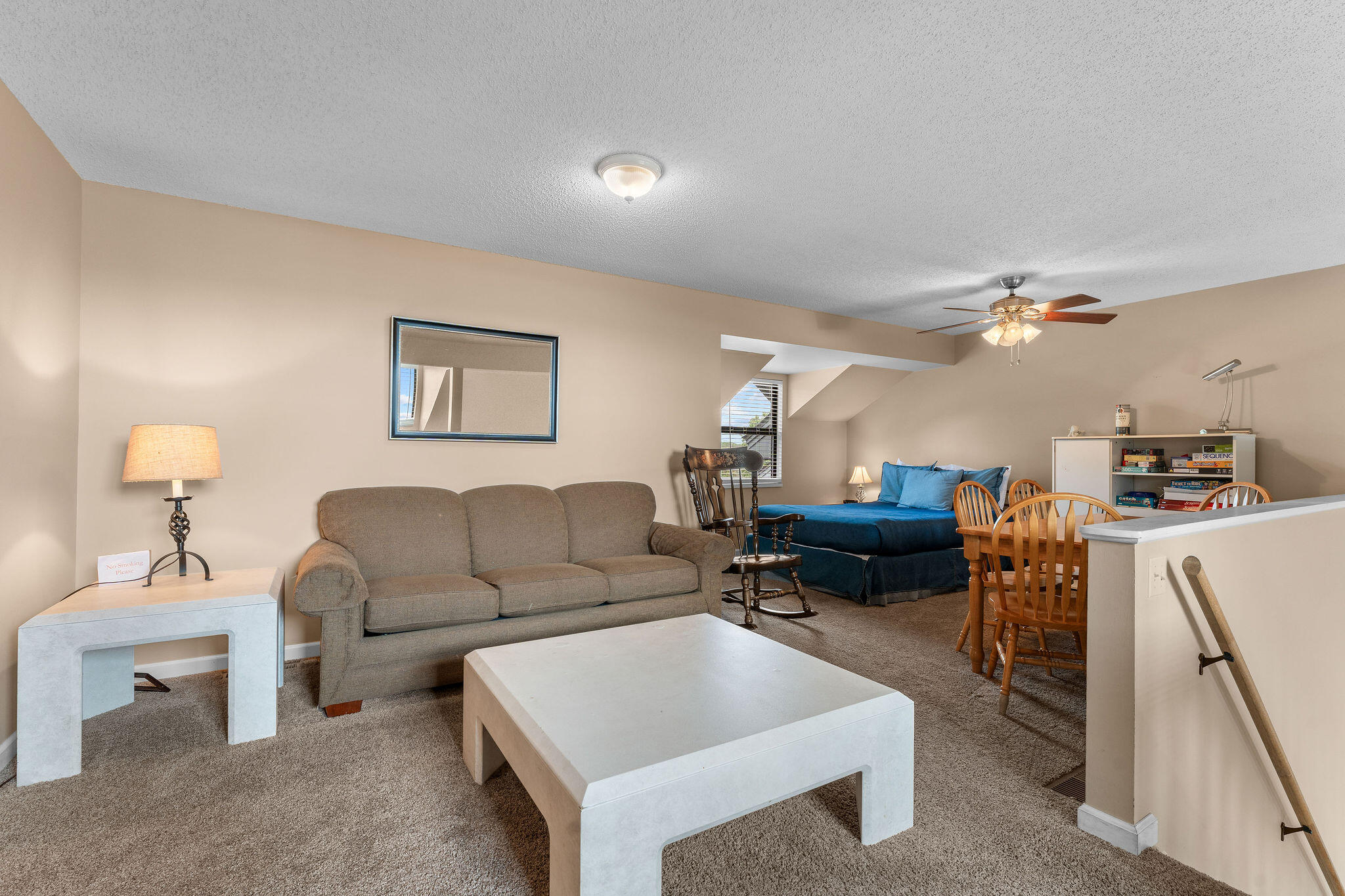Furnished living area with a gray sofa, white coffee tables, blue bed, and wooden dining set.