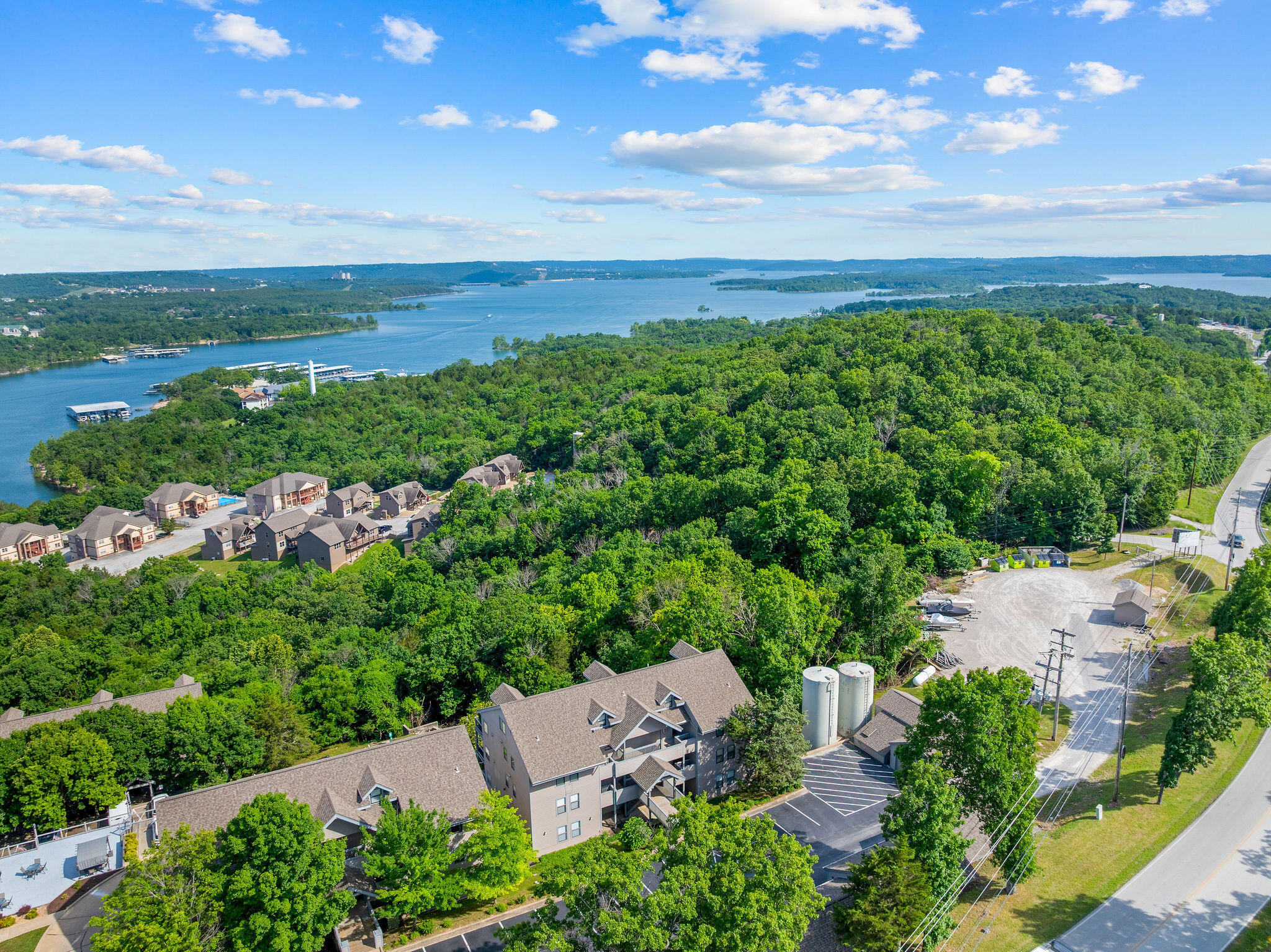 Aerial view of wooded condominium buildings beside a lake and curving road.