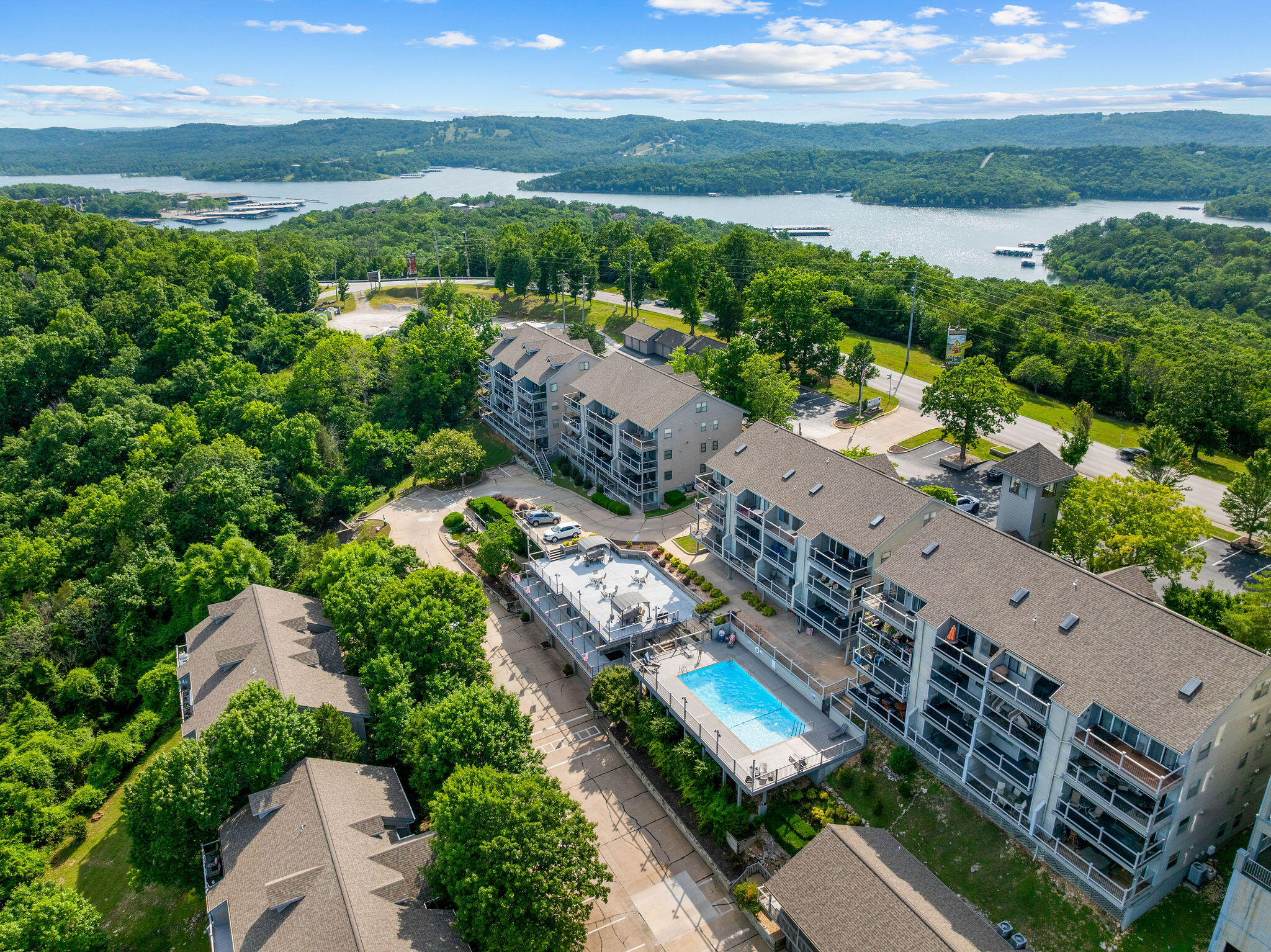 Condominium complex with an outdoor pool, surrounded by trees beside a lake.