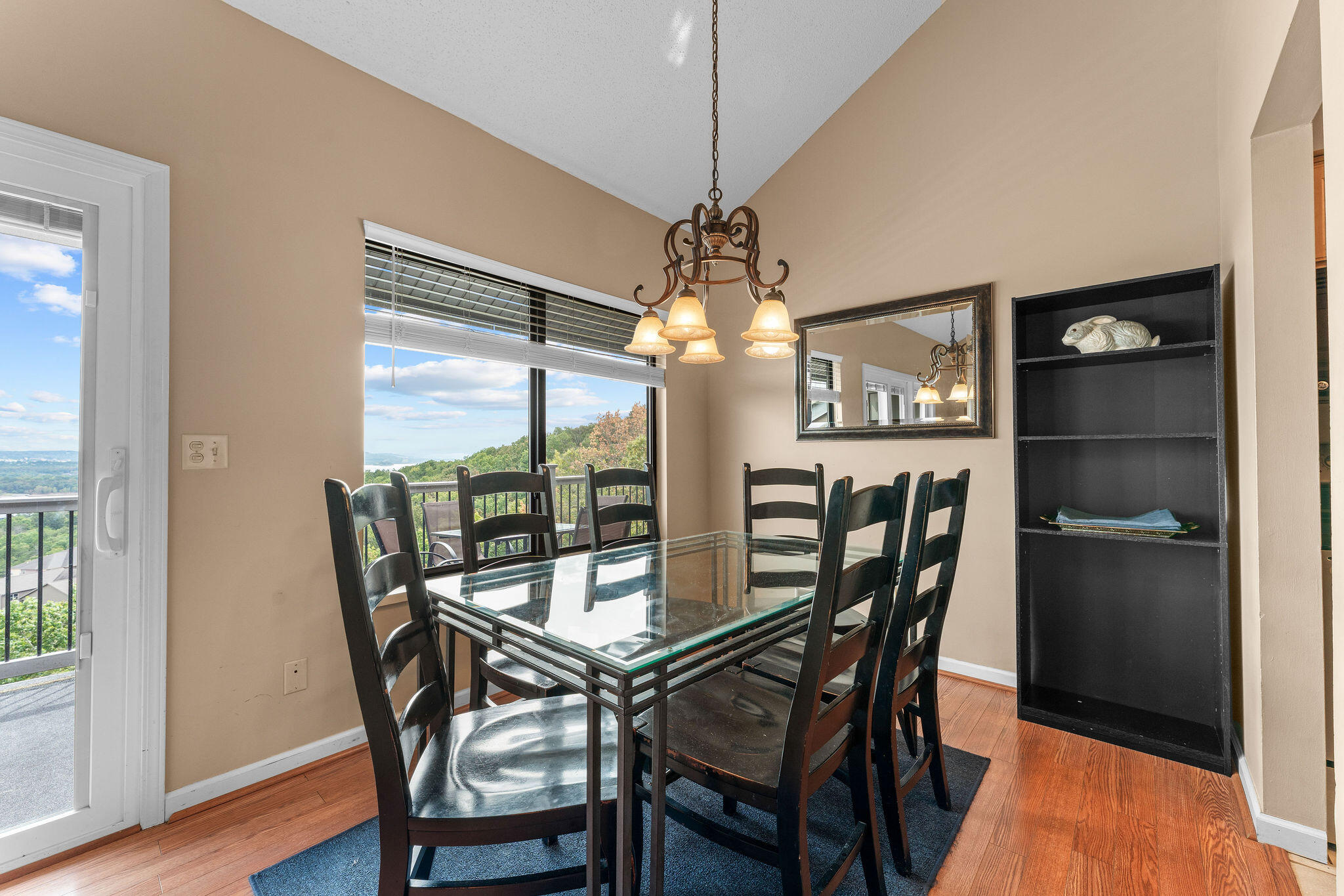 Dining room with a glass-top table, dark chairs, and a distant lake view through the windows.