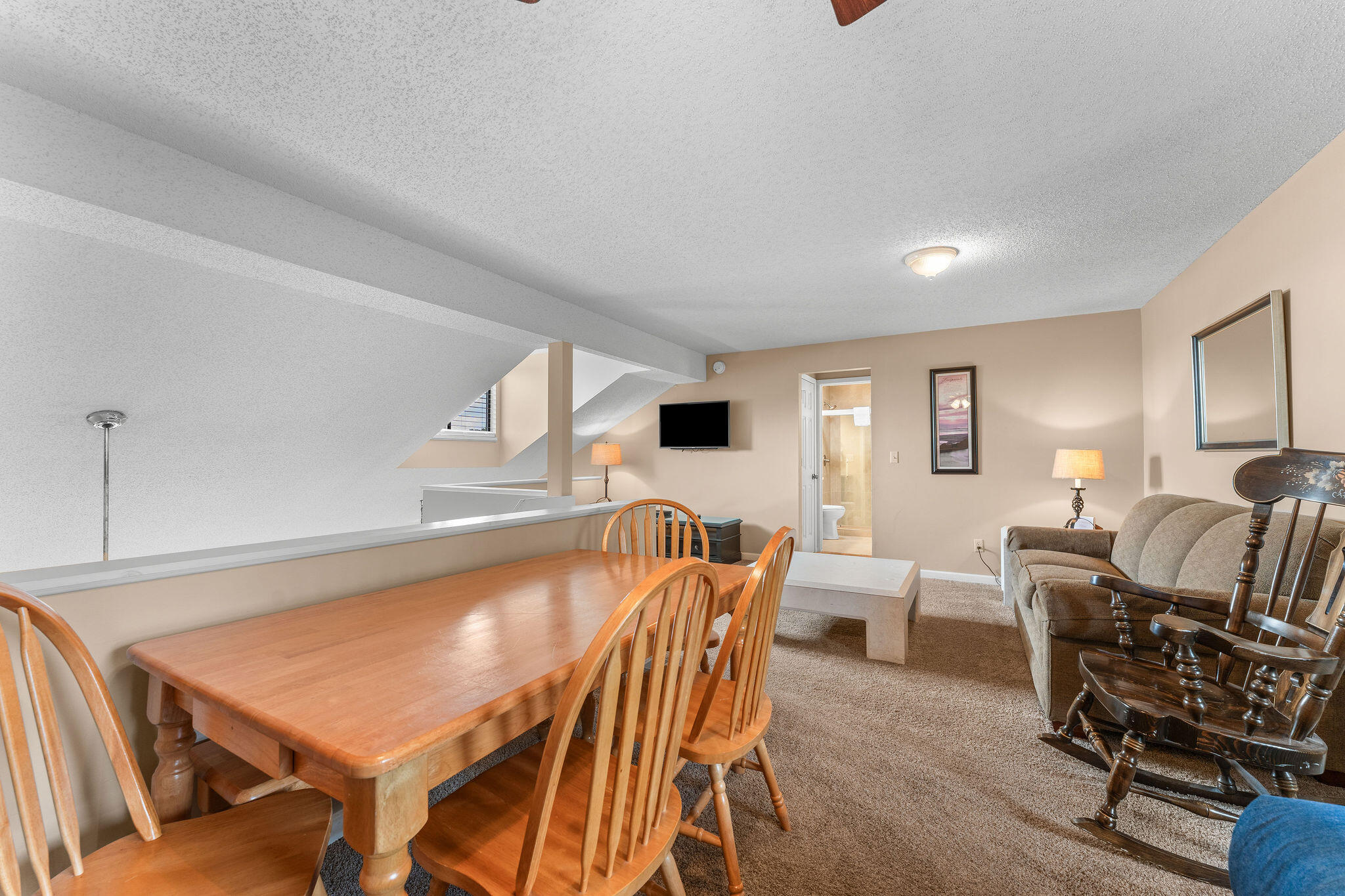 Dining and living area with a wooden table, beige sofa, and low sloped ceiling.