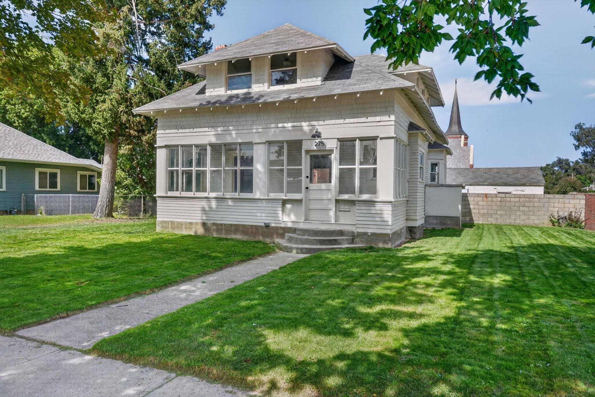 White two-story house with a wide enclosed porch, front walkway, and green lawn.