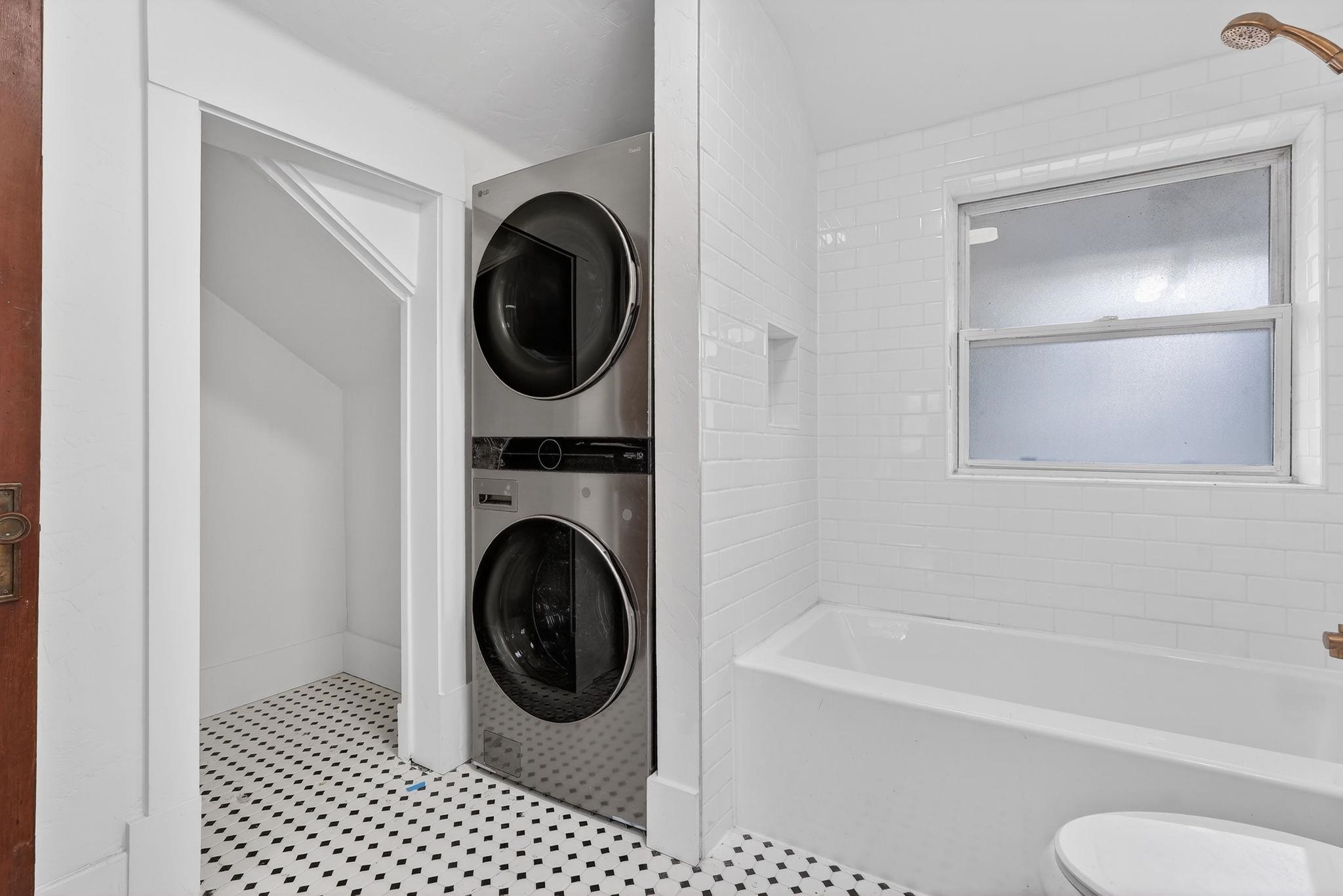 Bathroom with a bathtub and frosted window beside a stacked washer and dryer.