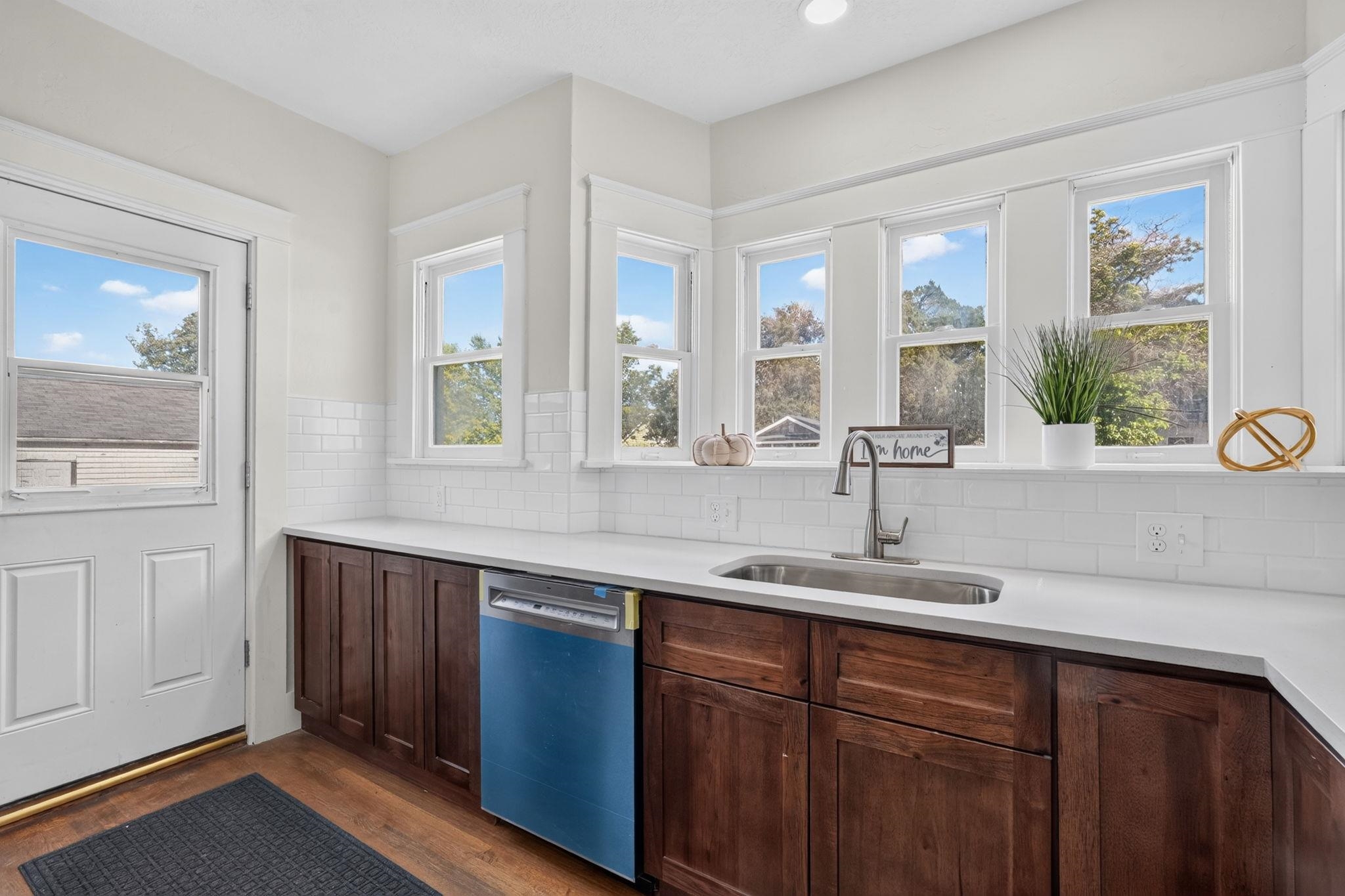 Kitchen with dark wood cabinets, white tile backsplash, stainless sink, and a row of large windows.
