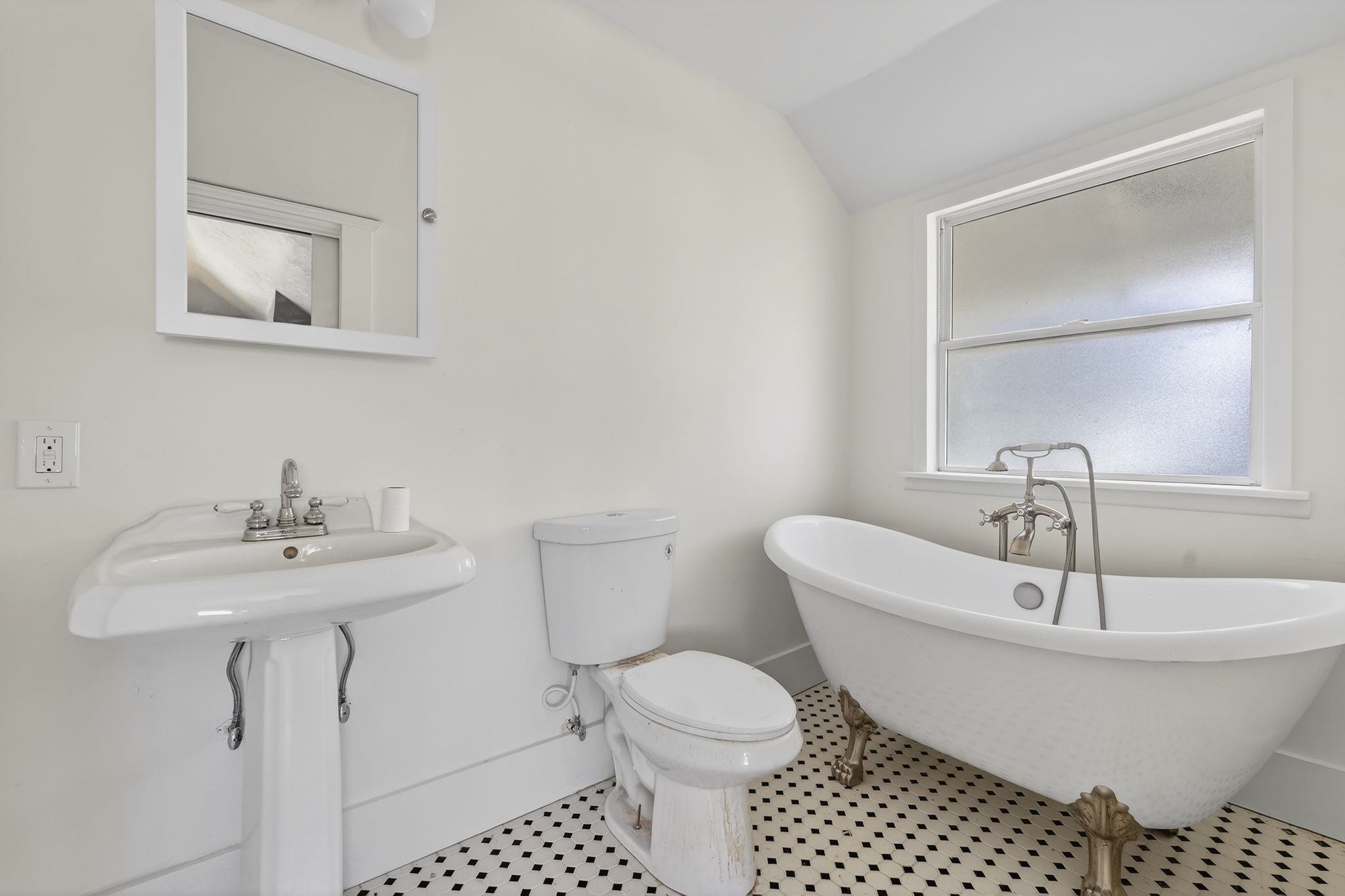 White bathroom with a clawfoot tub, pedestal sink, and black-and-white patterned floor.