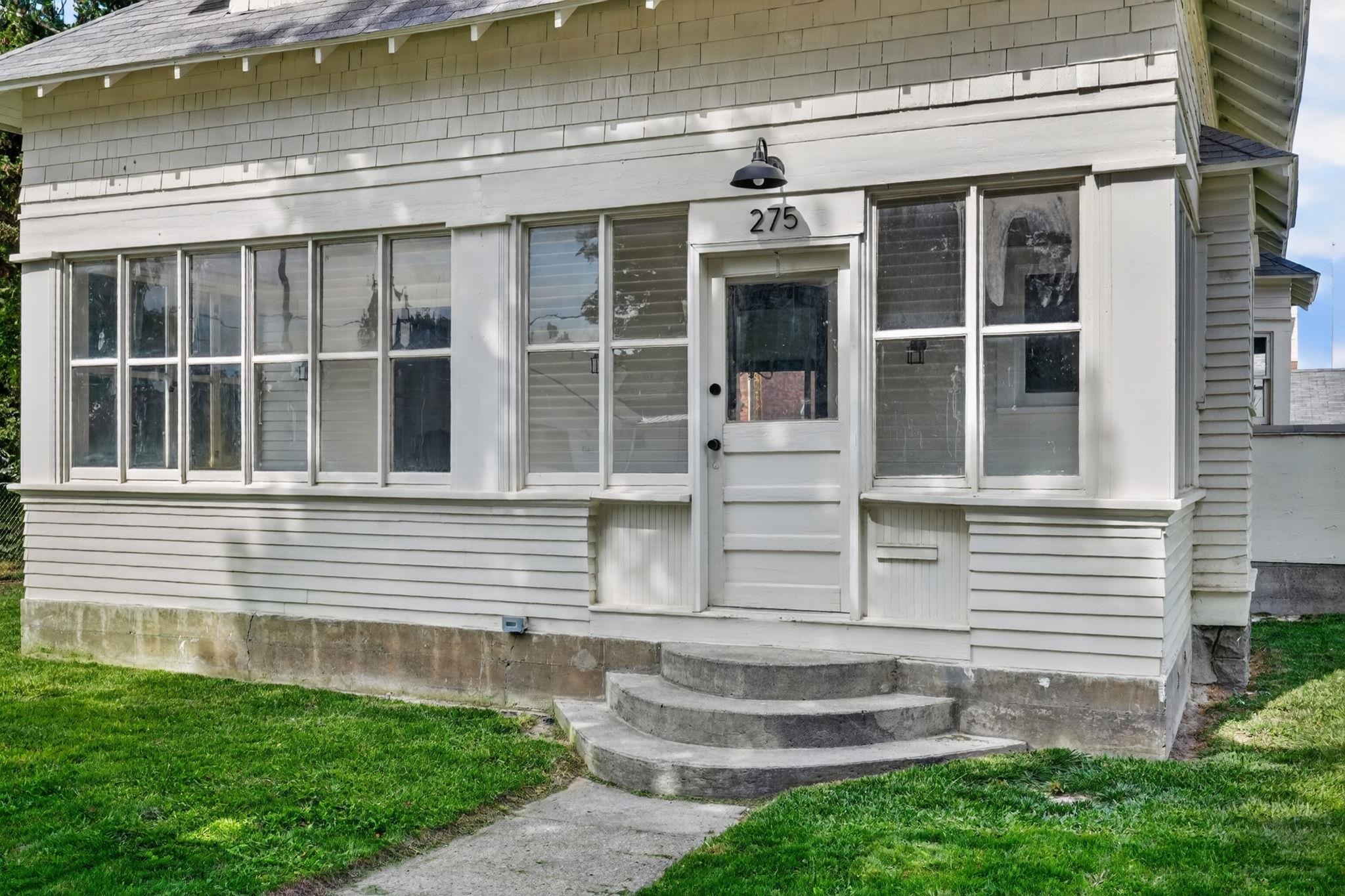 White-sided house entrance with broad windows, curved concrete steps, and the number 275 above the door.