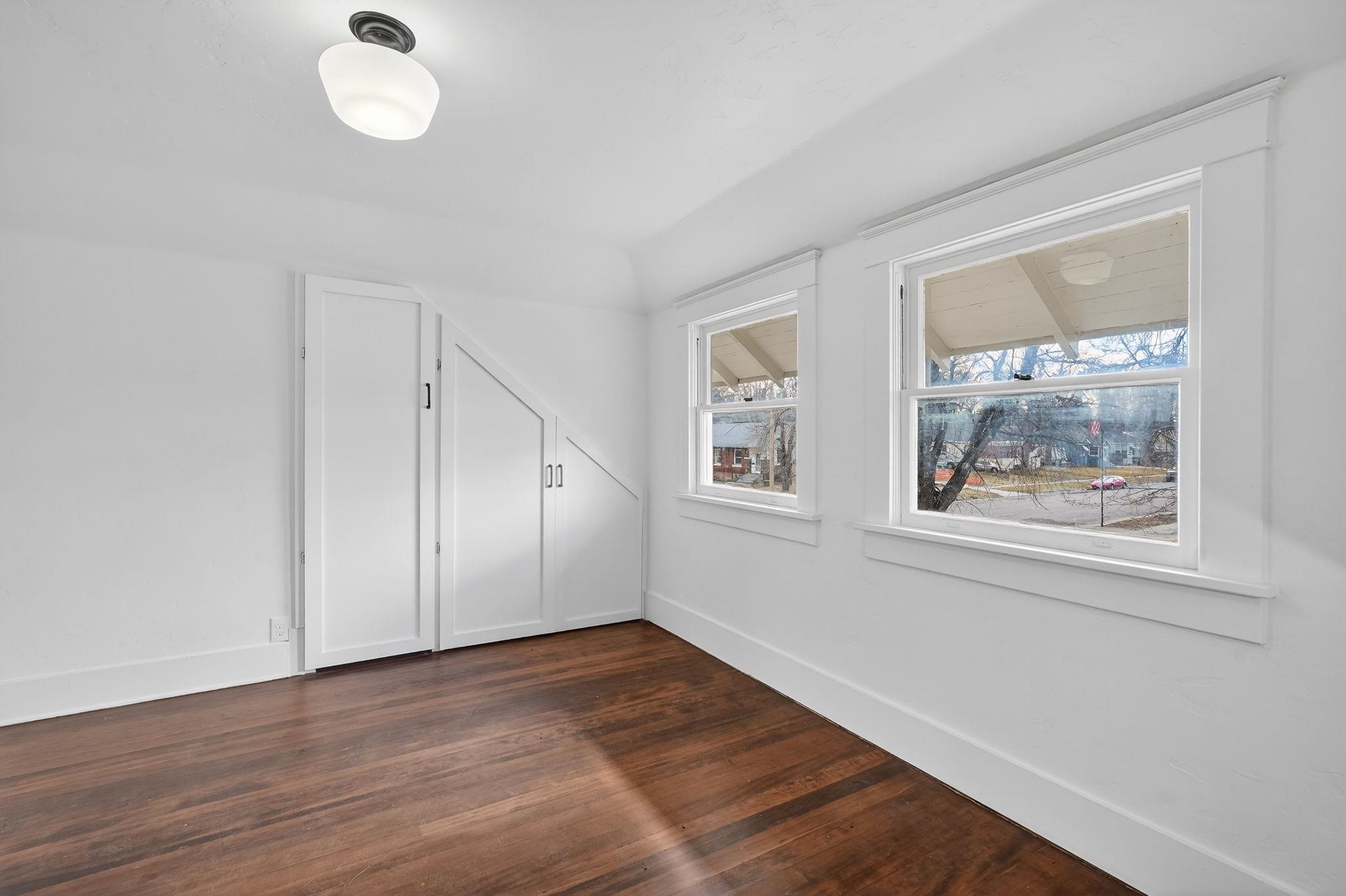 Vacant room with hardwood floors, large windows, and built-in storage beneath the stairs.