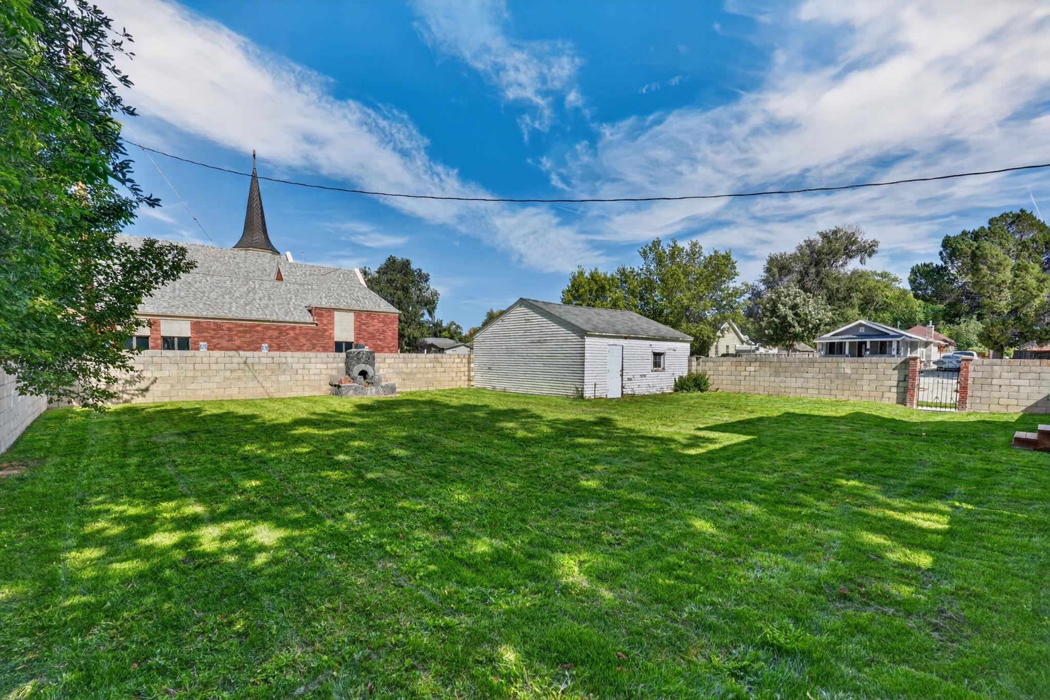 Backyard with a broad lawn, block wall, white shed, and metal gate.