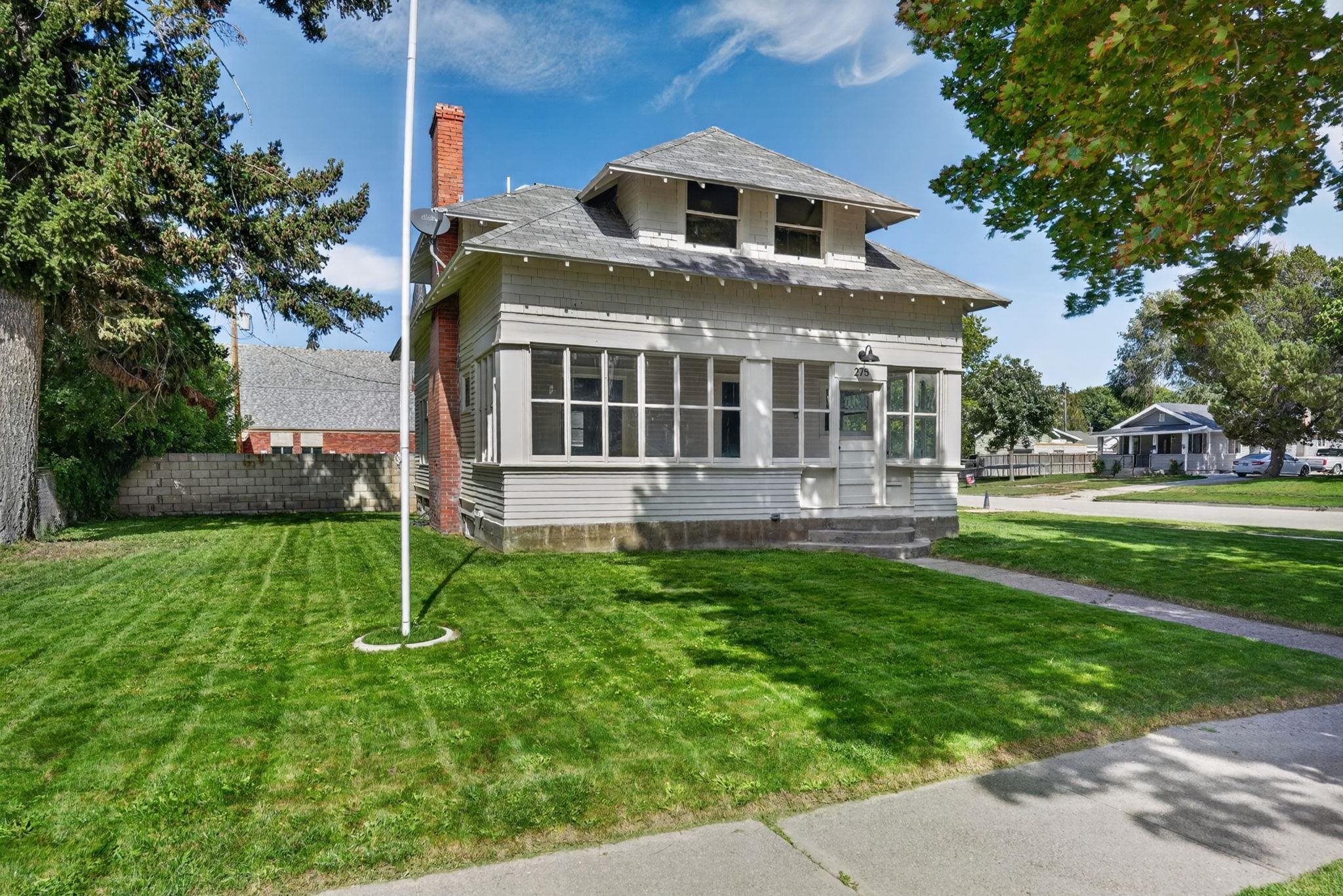 Two-story gray house with an enclosed front porch, brick chimney, and green lawn.