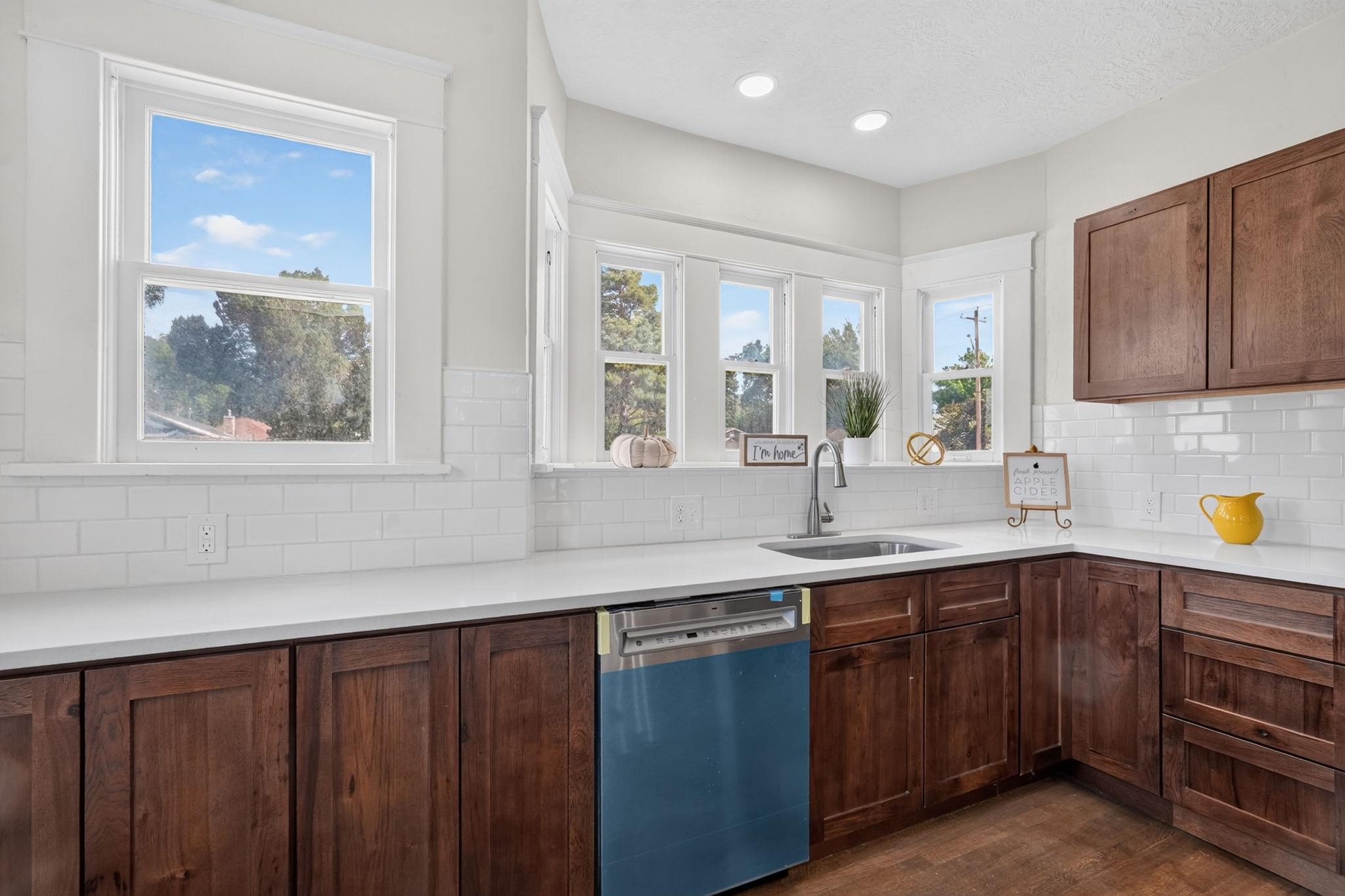 Bright kitchen with dark wood cabinets, white subway tile, and a sink beneath a row of windows.