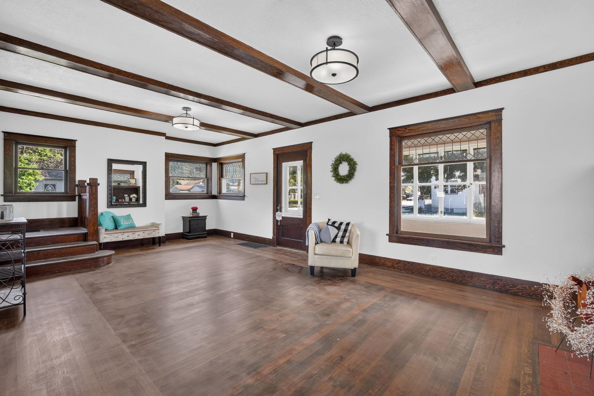 Living room with exposed dark wood ceiling beams, leaded-glass windows, and polished wood floors.