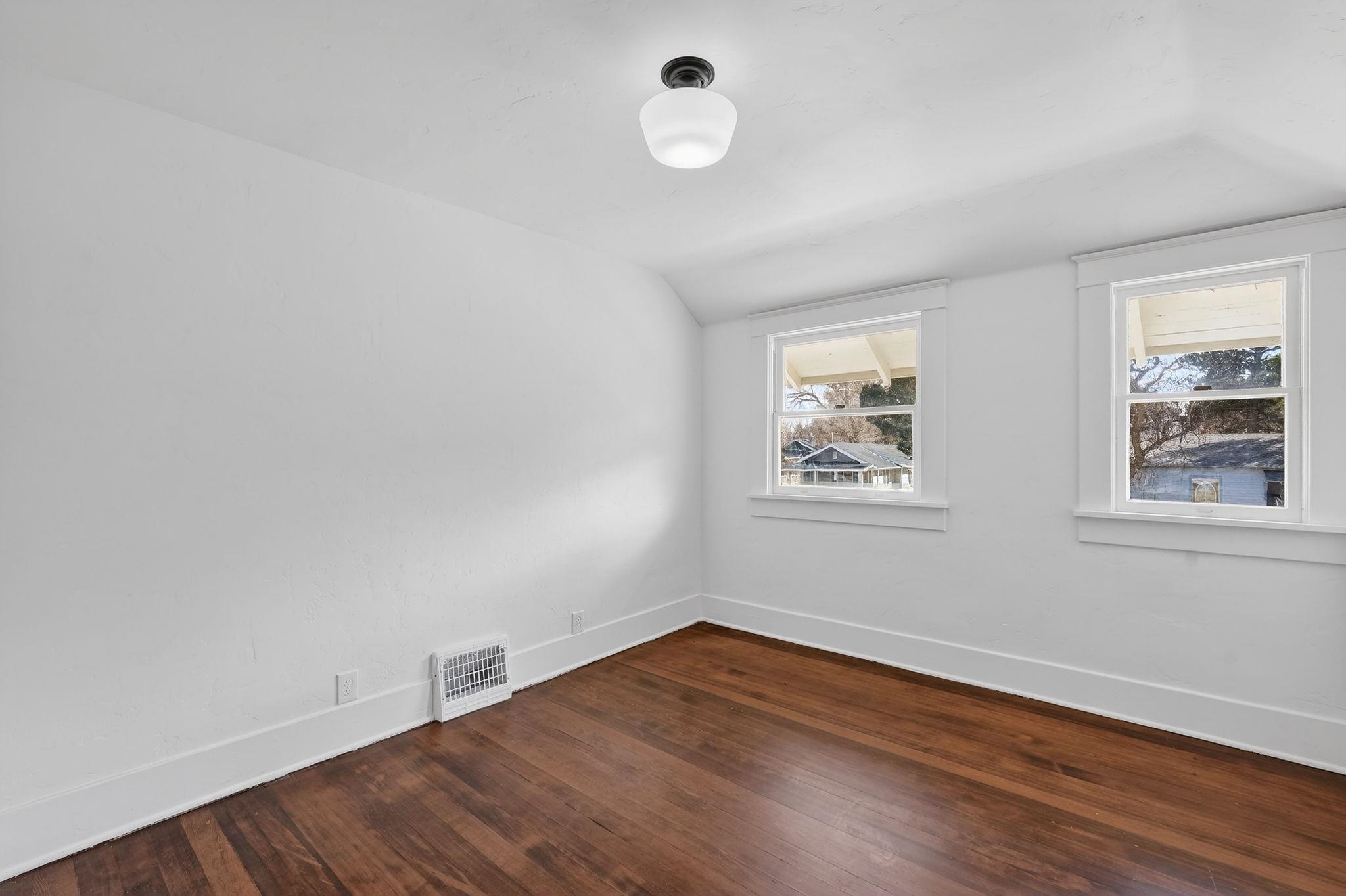 Empty room with dark wood floors, white walls, two windows, and a small wall heater.