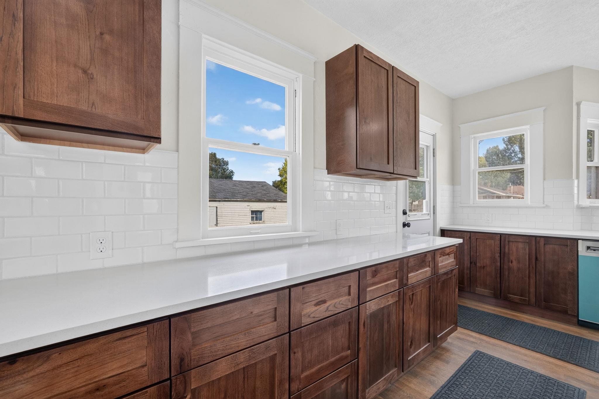 Kitchen with dark wood cabinetry, white counters, subway tile backsplash, and several bright windows.