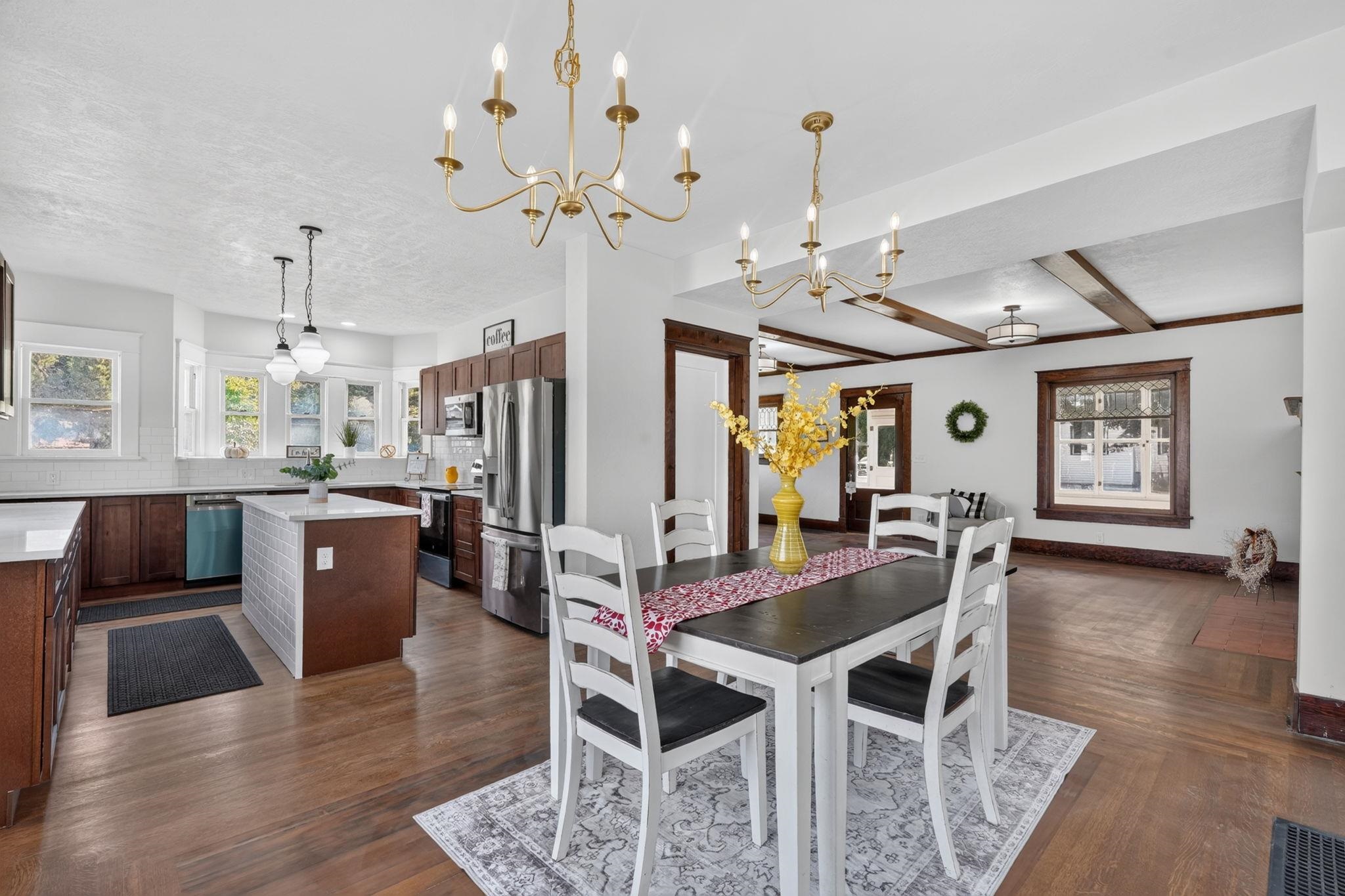 Open kitchen and dining area with dark wood cabinets, a tiled island, and brass chandeliers.